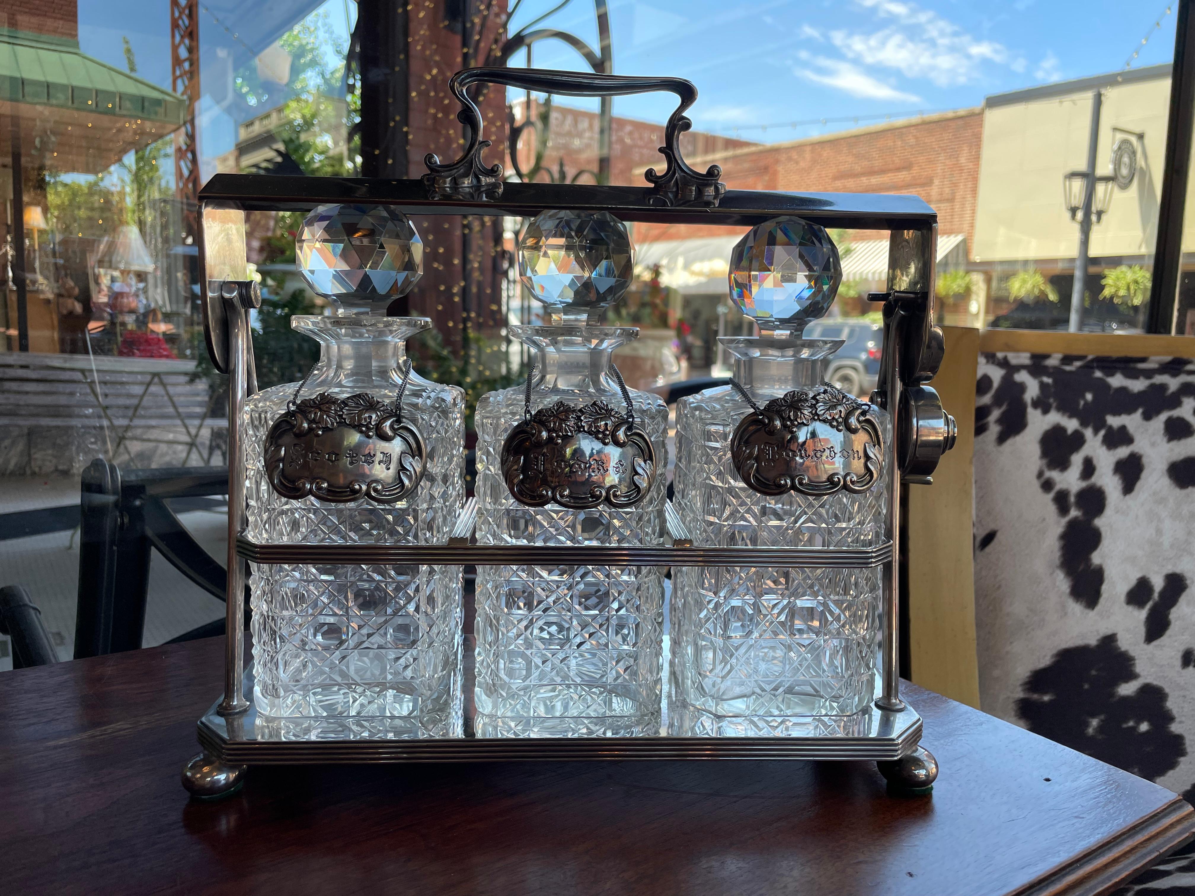 Entertain in style with this 19th century English silver plated three carafe tantalus in good used condition.  
Scotch, Vodka and Bourbon signs are included with the cut glass decanters.
The locking mechanism holds the bottles in place for easy