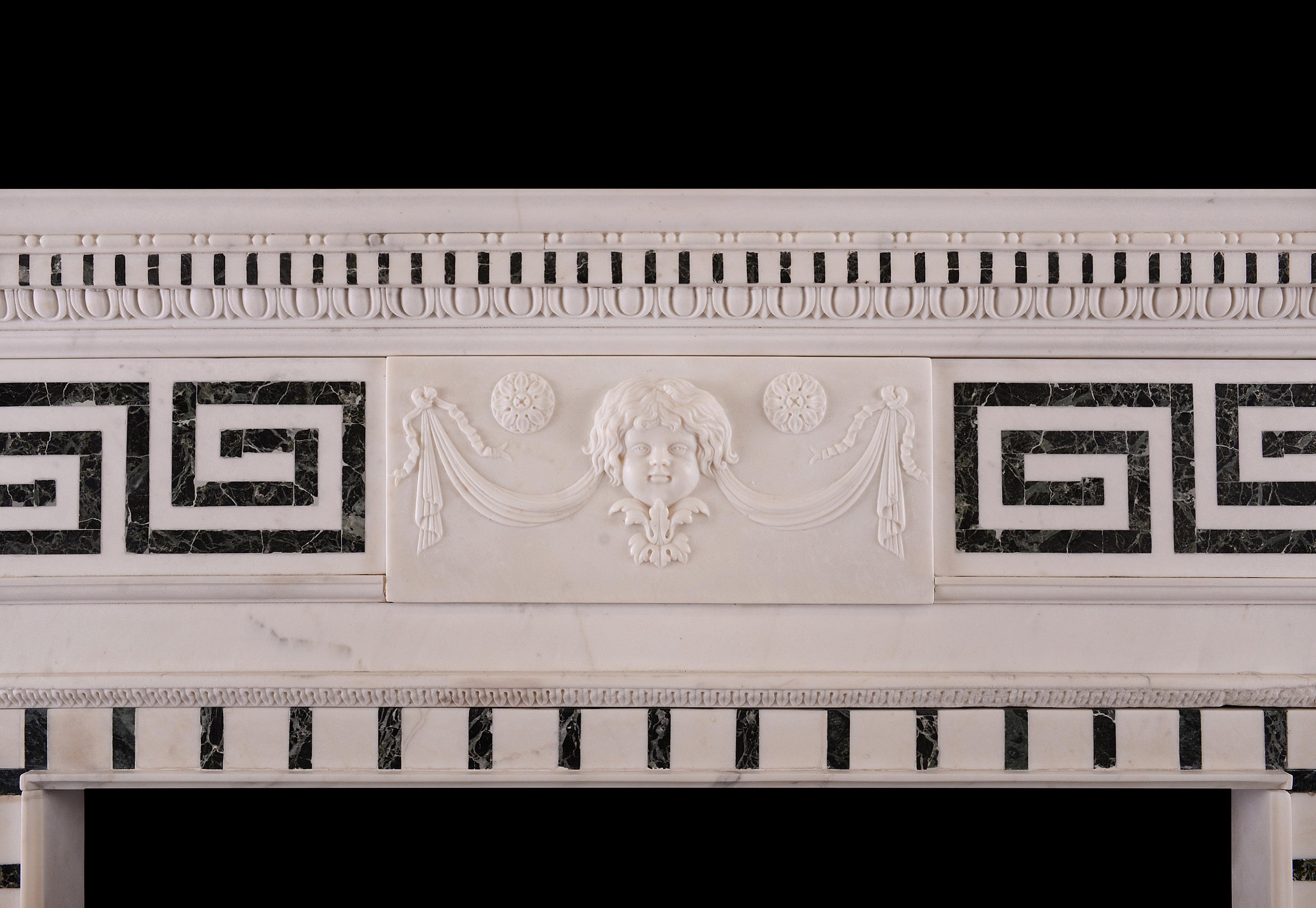 A 19th century English statuary and inlaid Tinos marble fireplace, with carved mask and drapery centre tablet, inlaid Greek key side panels, fluted Tinos marble jambs with oval patera surmounted by urn side blockings, and inlaid dentil cornice and