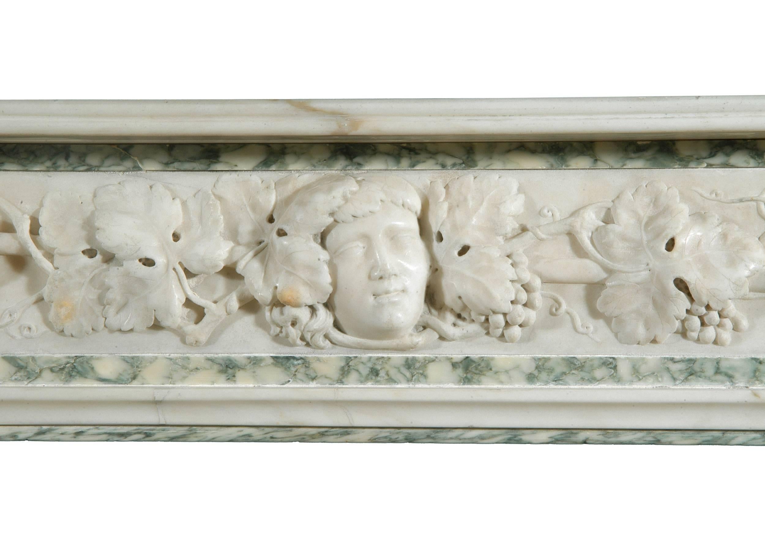 A 19th century (circa 1850) English statuary and Vert d'Estours marble fireplace, with heavily carved frieze of intertwined vine leaves around carved staff, theatrical mask to centre. The jambs carved with leaves and bellflowers. Reeded moulded