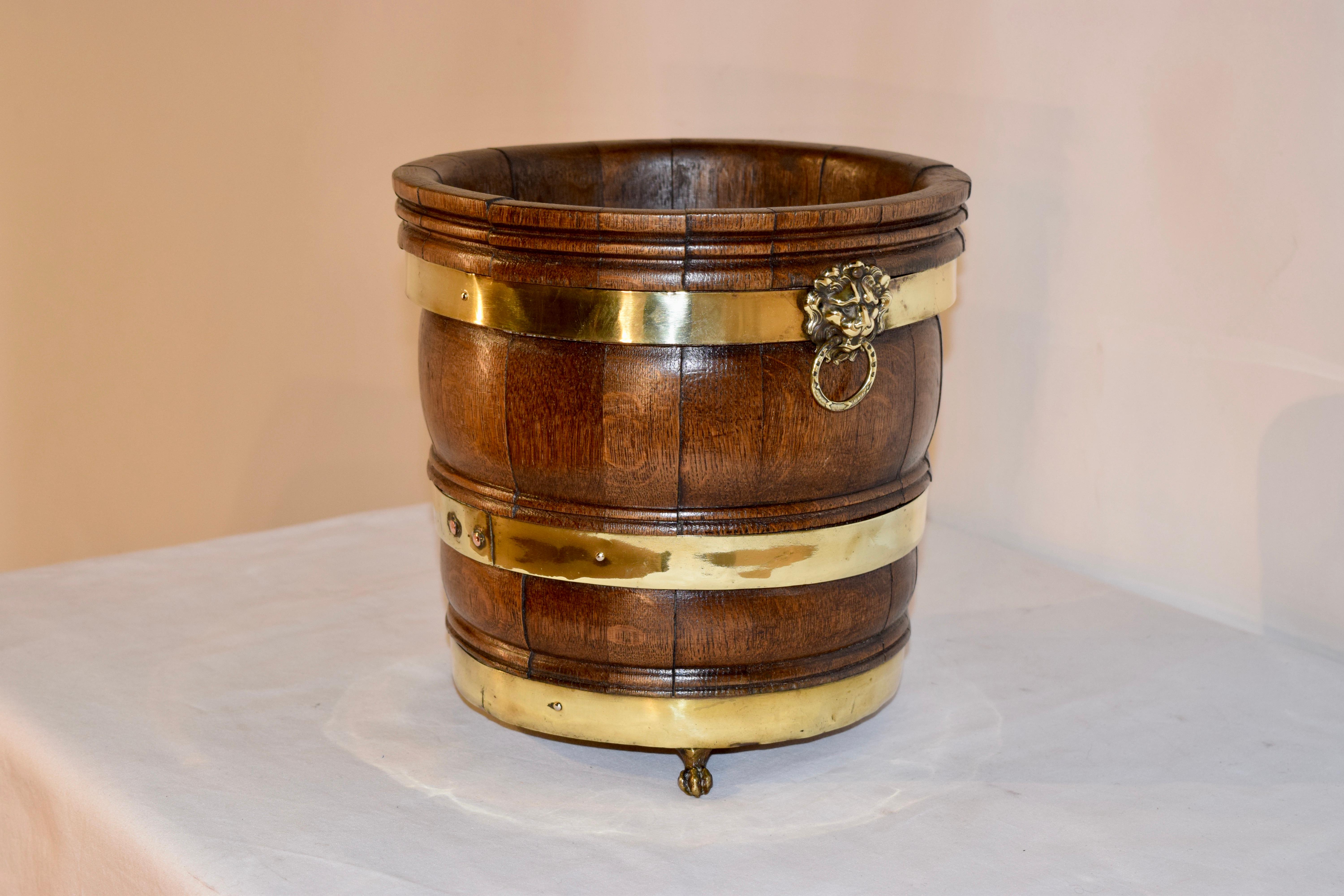 19th century strapped planter from England made from molded oak staves and strapped with brass belts. It has hand cast brass lion's head handles on the sides and is supported on cast brass feet.