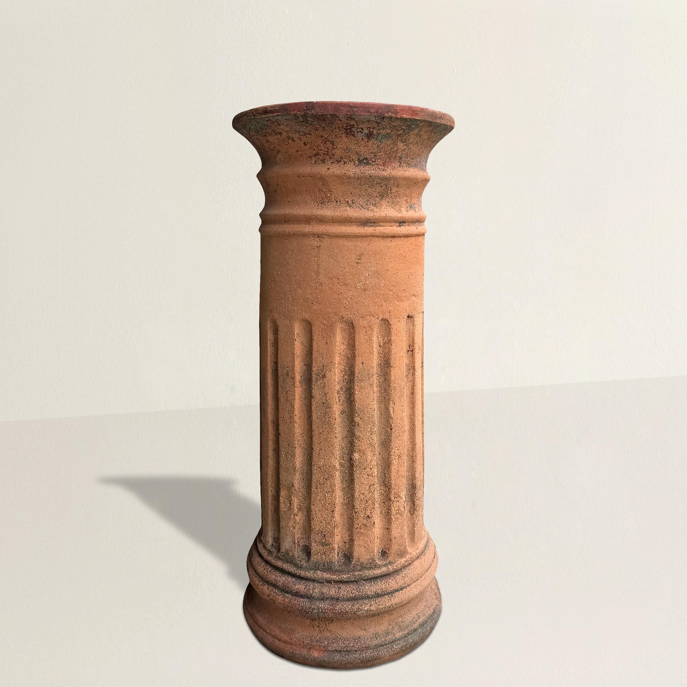 A striking 19th-century English terracotta chimney pot, beautifully weathered by time and the elements. Crafted in the form of a classical fluted column, this architectural relic exudes old-world charm with its slightly tapered silhouette and rich