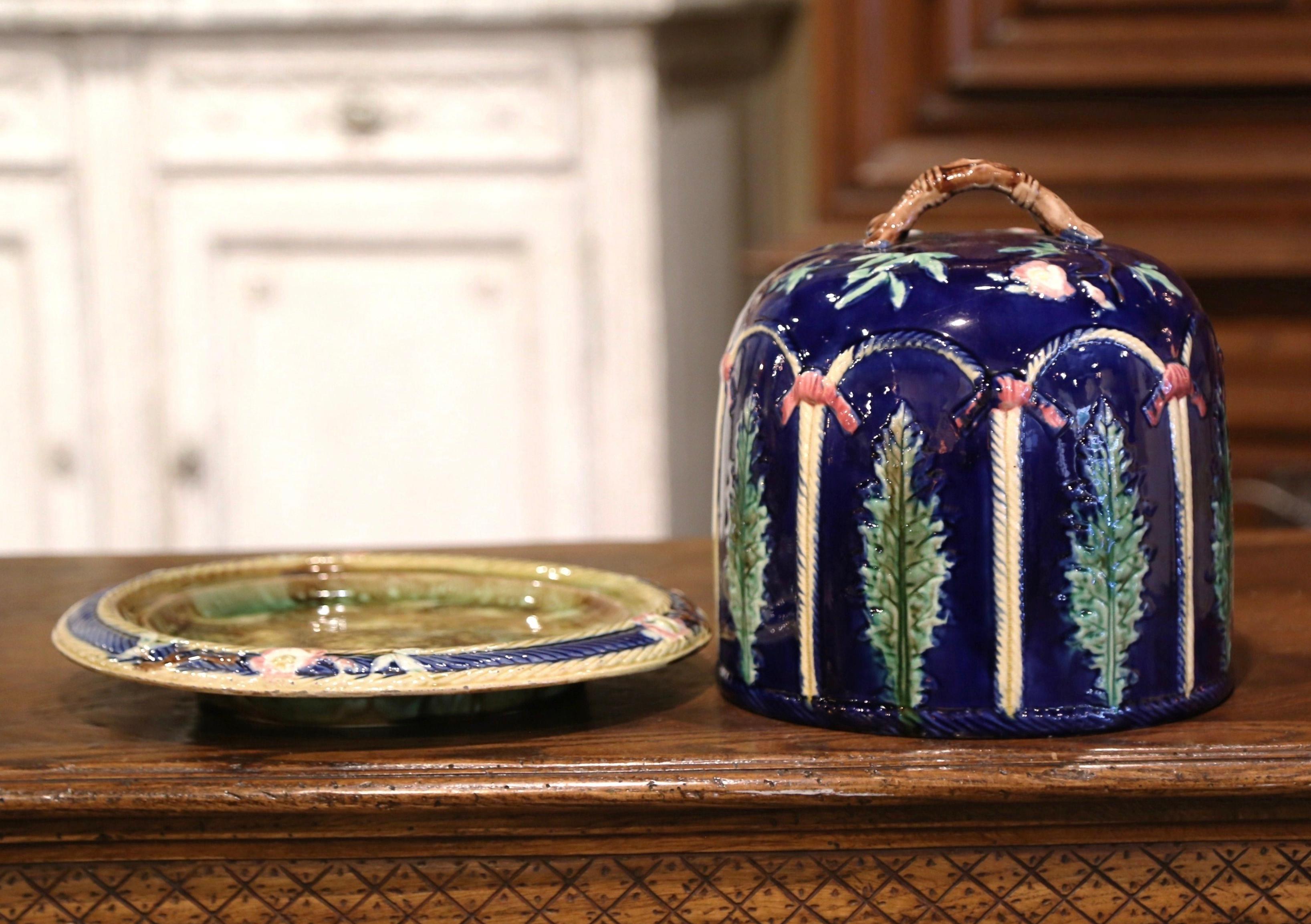 This colorful two-piece antique Majolica cheese dome was crafted in England, circa 1870. Attributed to Thomas Forester, the dish includes a cobalt blue and green circular platter bottom with molded border, and decorated with floral and leaf motifs.
