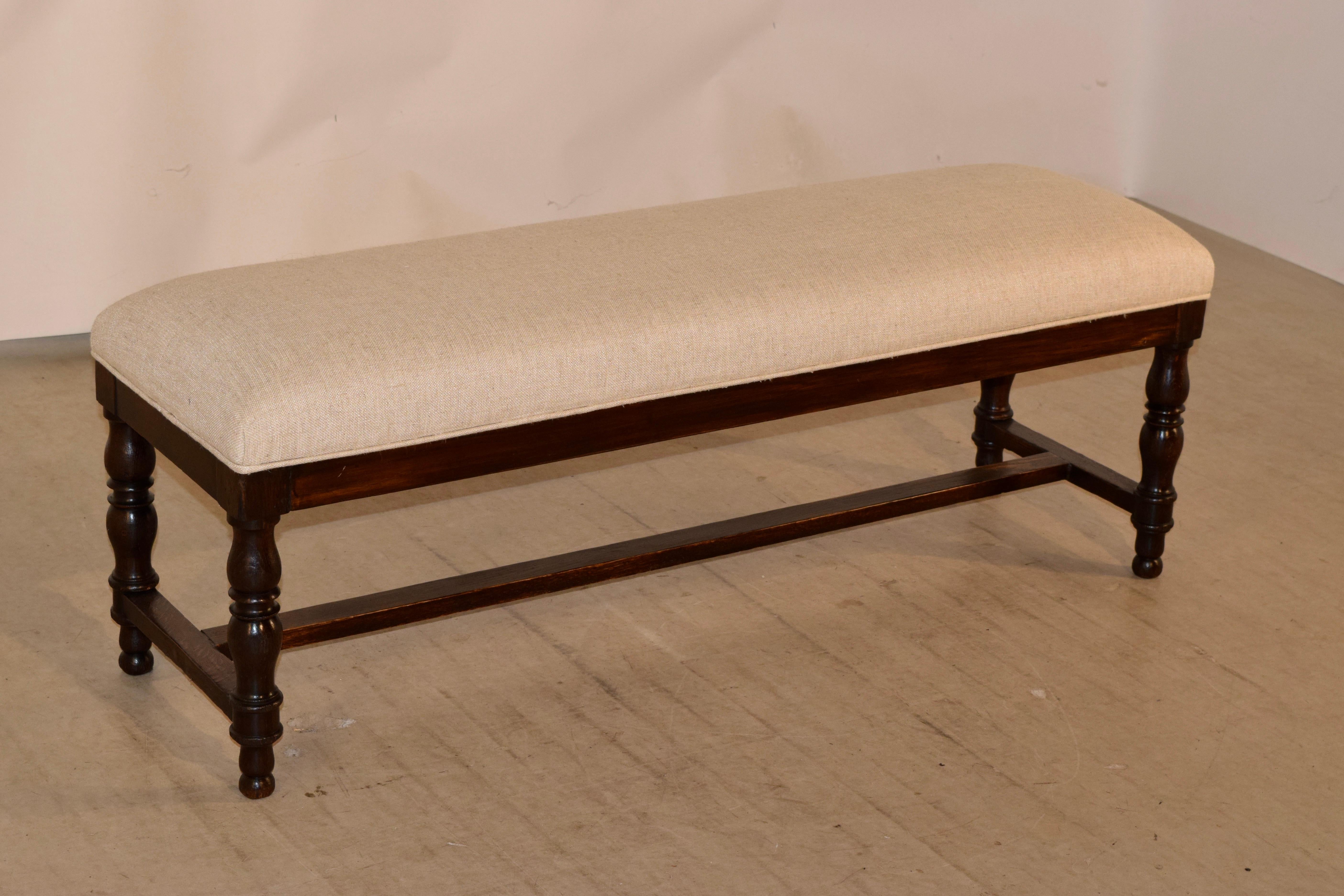 19th century English oak bench with newly upholstered seat in linen, which is finished with a single welt and is supported on hand turned legs, joined by cross stretchers. Simple and elegant.