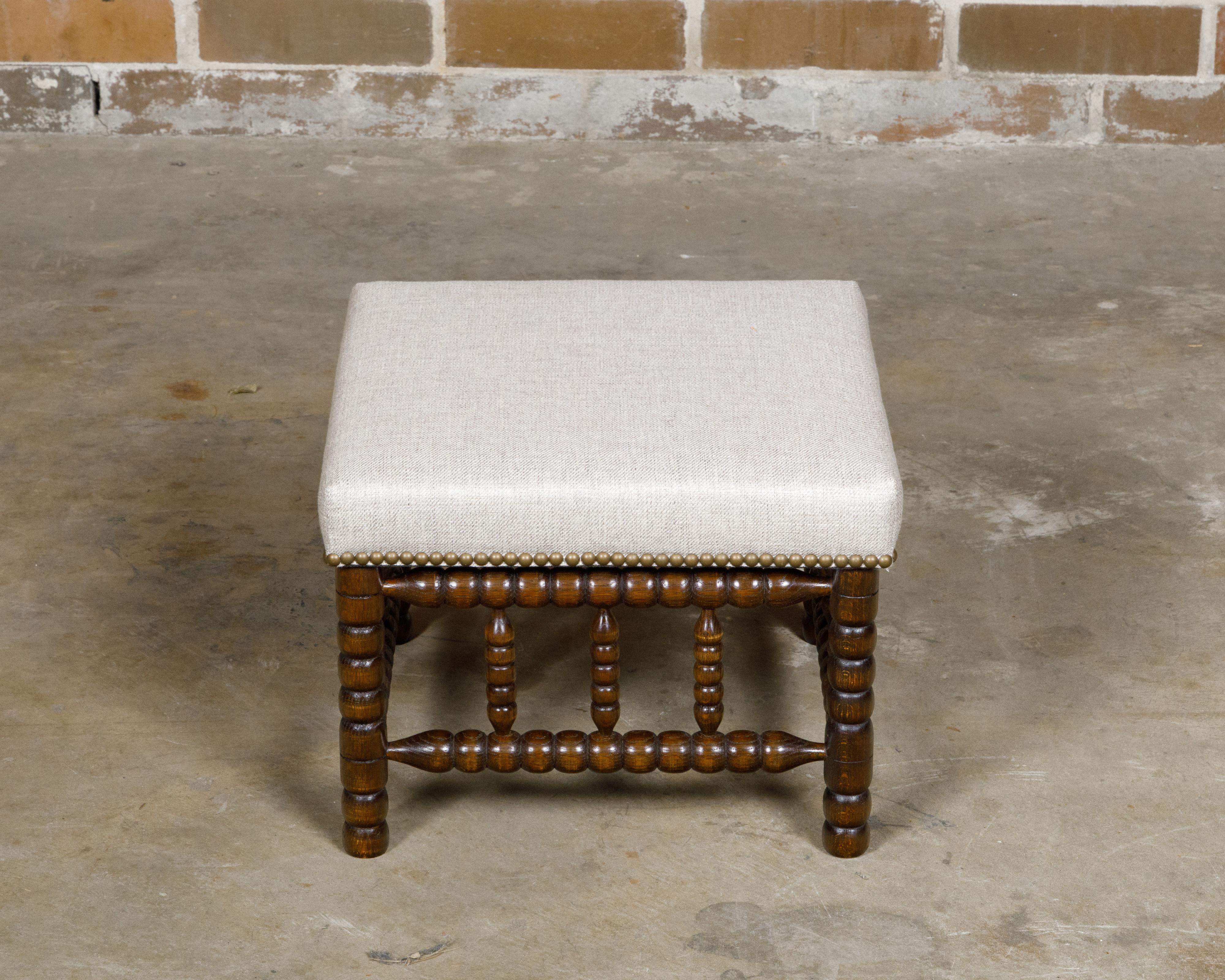Uno sgabello inglese con gambe a rocchetto del XIX secolo con una nuova tappezzeria in lino fissata con una bordura di chiodi in ottone. Questo sgabello inglese con gamba a rocchetto del XIX secolo cattura l'essenza dell'artigianato senza tempo e