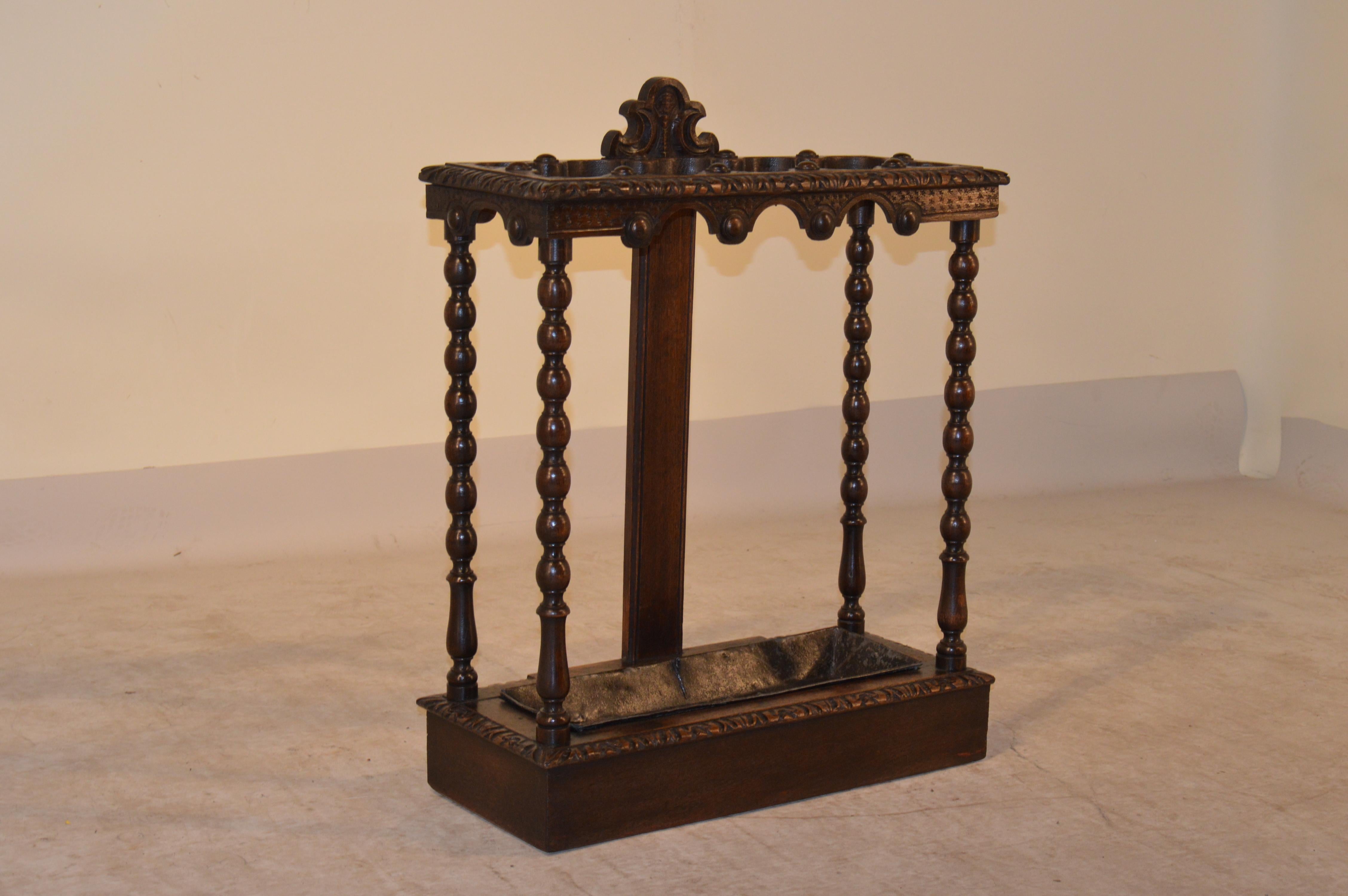 19th century English oak umbrella stand with a heavily carved top which is scalloped in sections for umbrella or cane storage. The apron is scalloped and carved to match. The legs are hand-turned in a spool design. The base is banded and has a