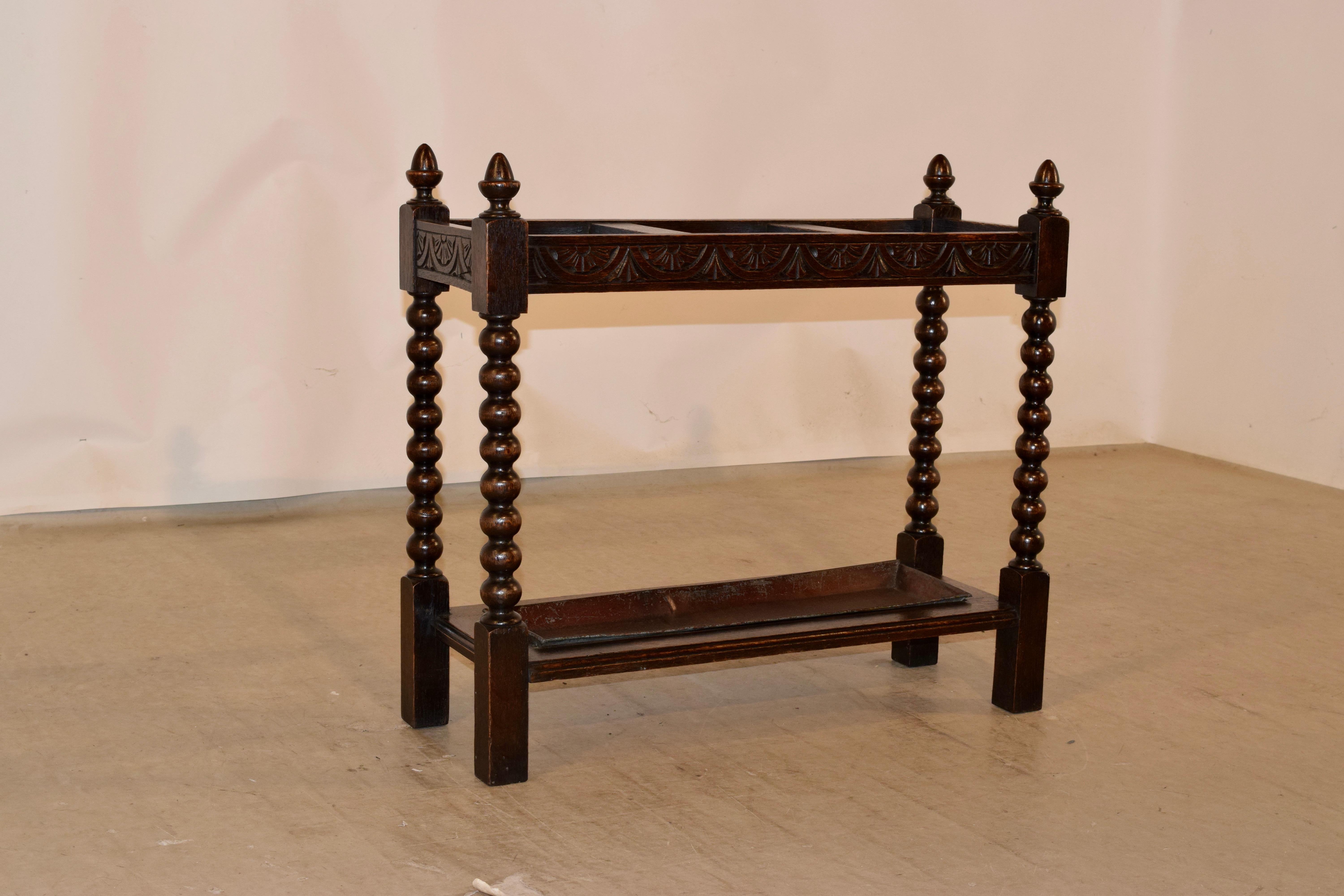 19th century oak umbrella stand from England. There are four hand turned finials over a top rail, which is hand carved with lunette design, supported on hand turned bobbin legs, which are connected by simple stretchers with molded edges, that