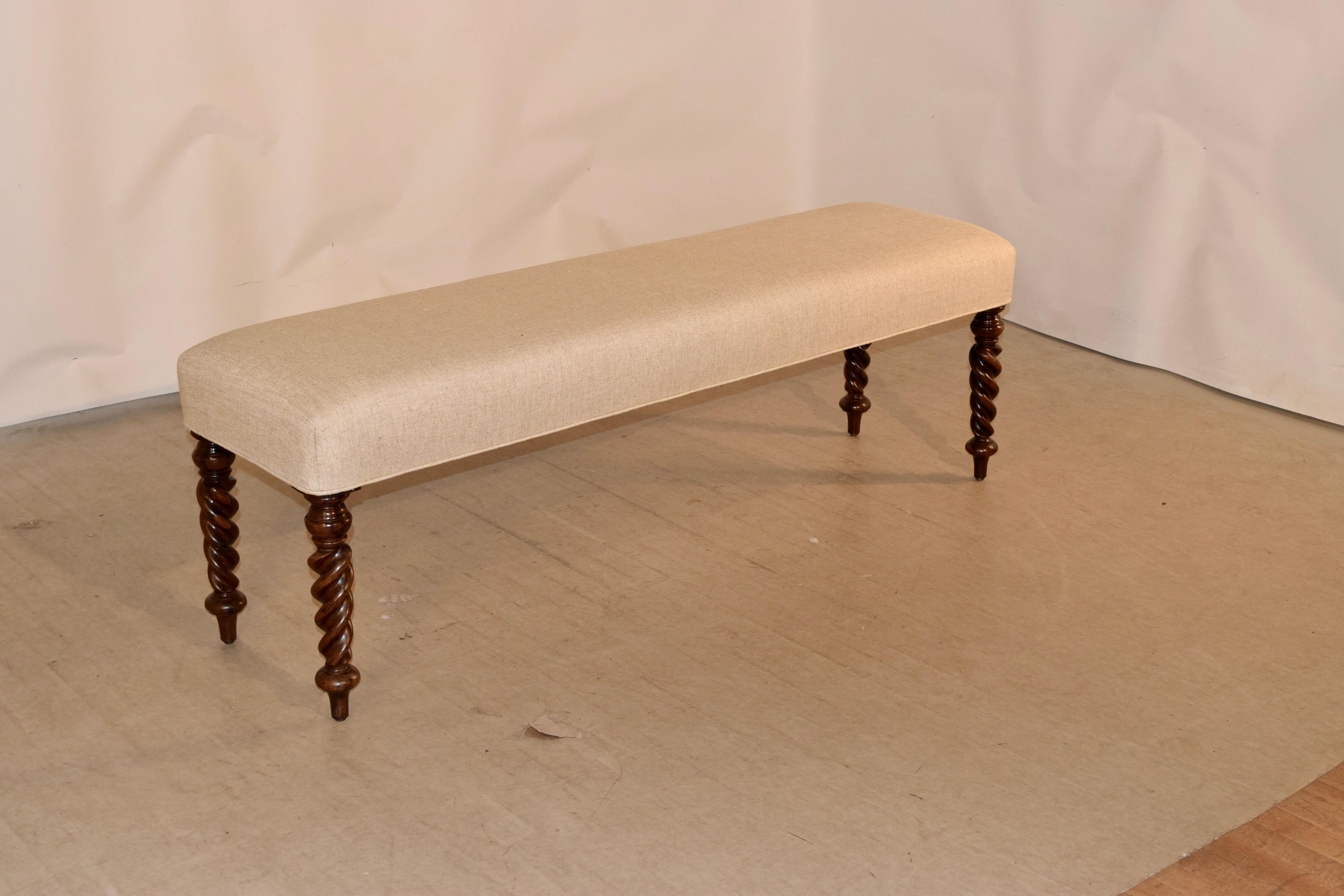 19th century upholstered bench from England with newly upholstered seat in linen finished with single welt decoration, supported upon mahogany hand-turned flame twist feet.
