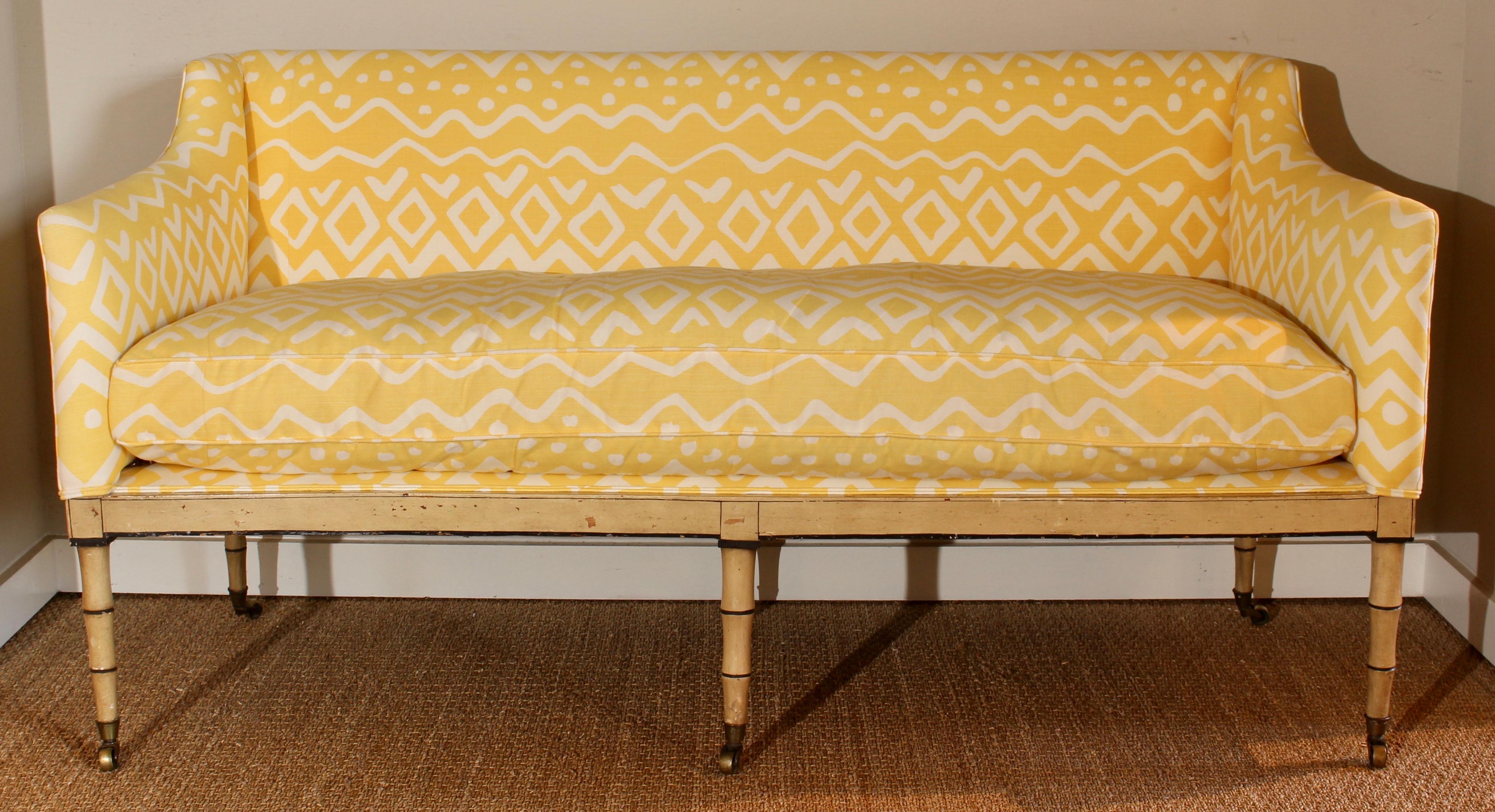 An early 19th century, English upholstered sofa with one long down filled cushion recently covered in a yellow linen fabric and resting on faux bamboo tapering legs terminating in brass cup casters.