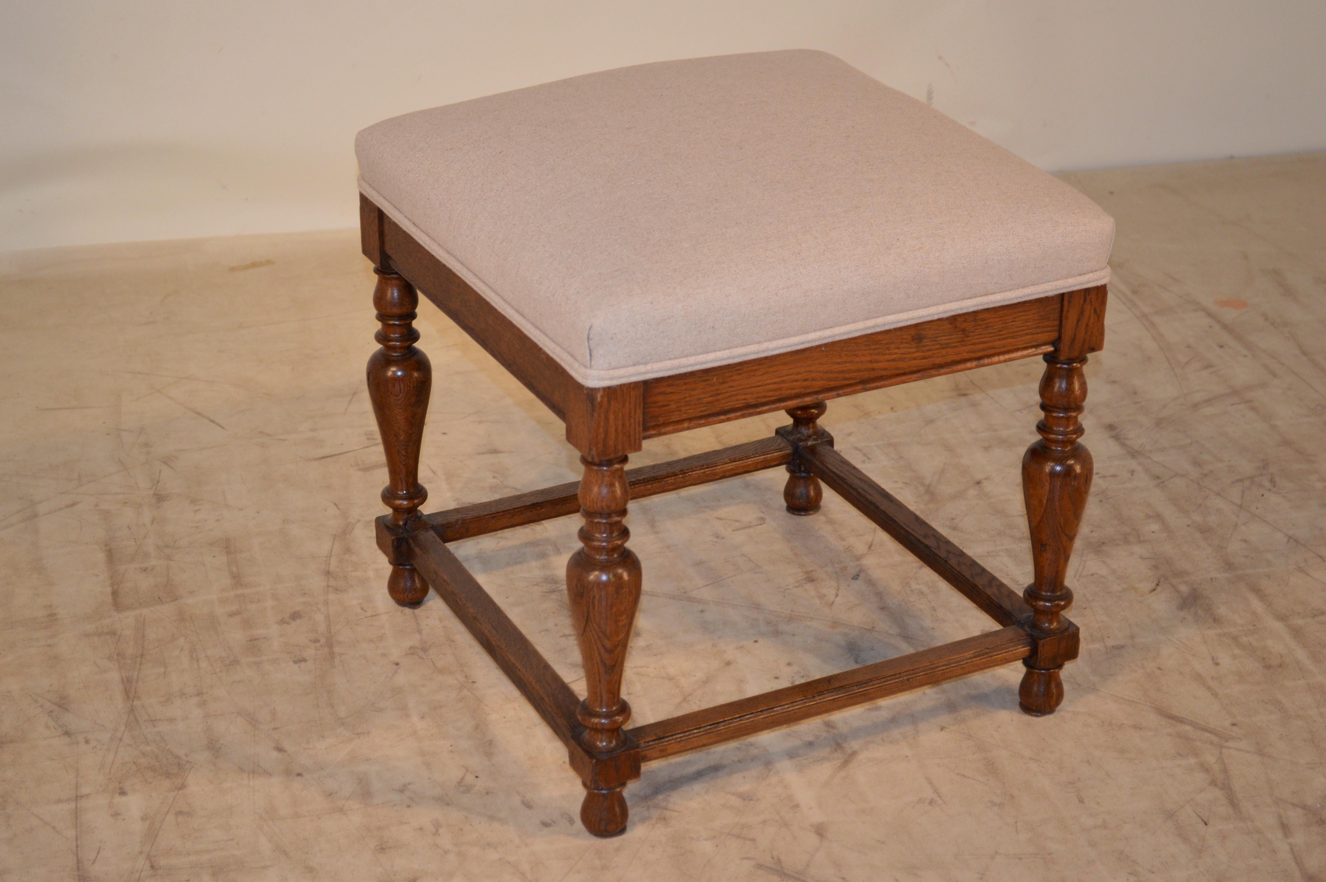 19th century English oak stool with hand-turned legs joined by stretchers and raised on turned feet. The seat is newly upholstered in linen and is finished with a double-welt decoration.