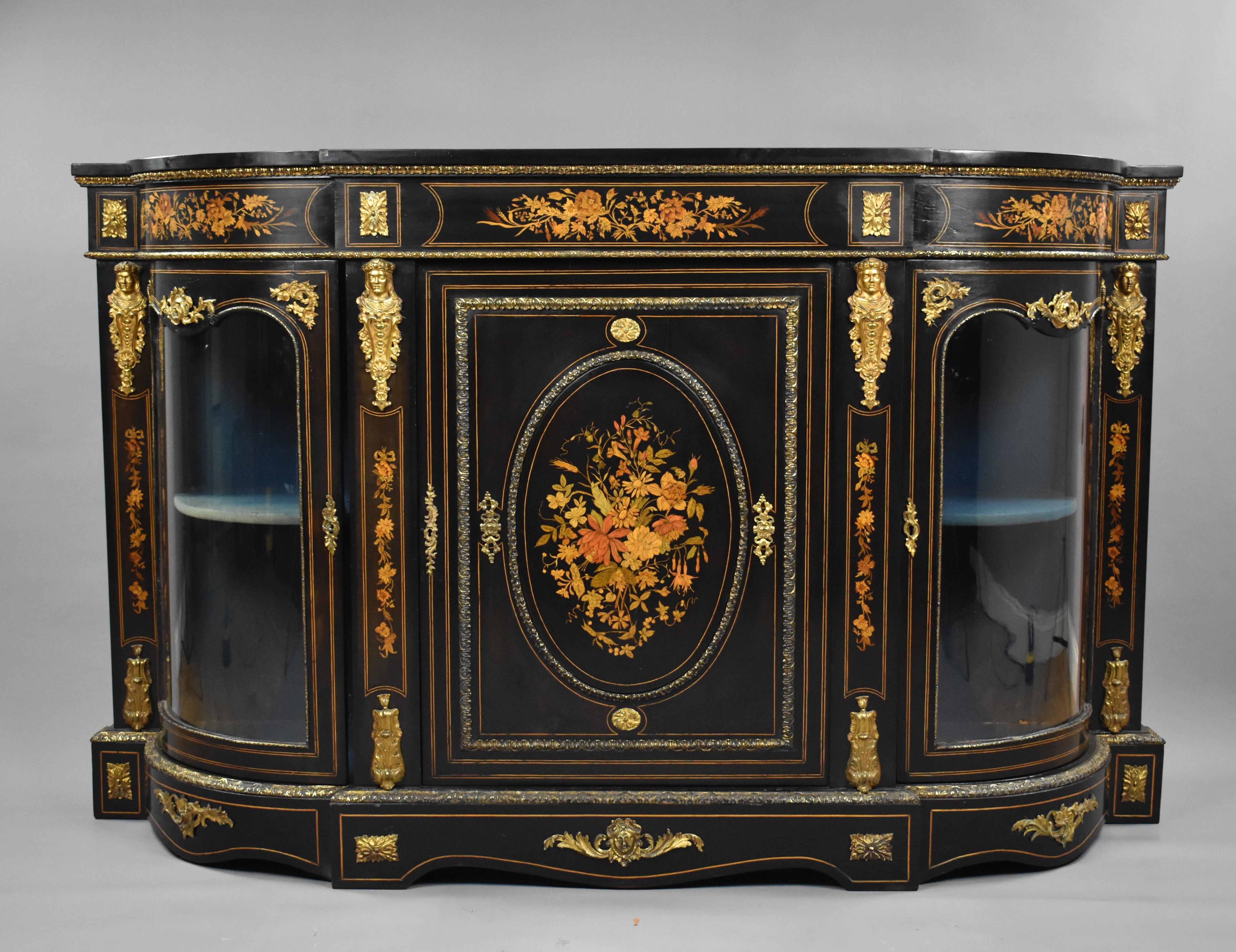 A good quality 19th century English Victorian ebonised and marquetry credenza, profusely inlaid with floral marquetry throughout and decorated with ormolu mounts, the credenza has two bowed glass doors flanking a central cupboard, above a shaped