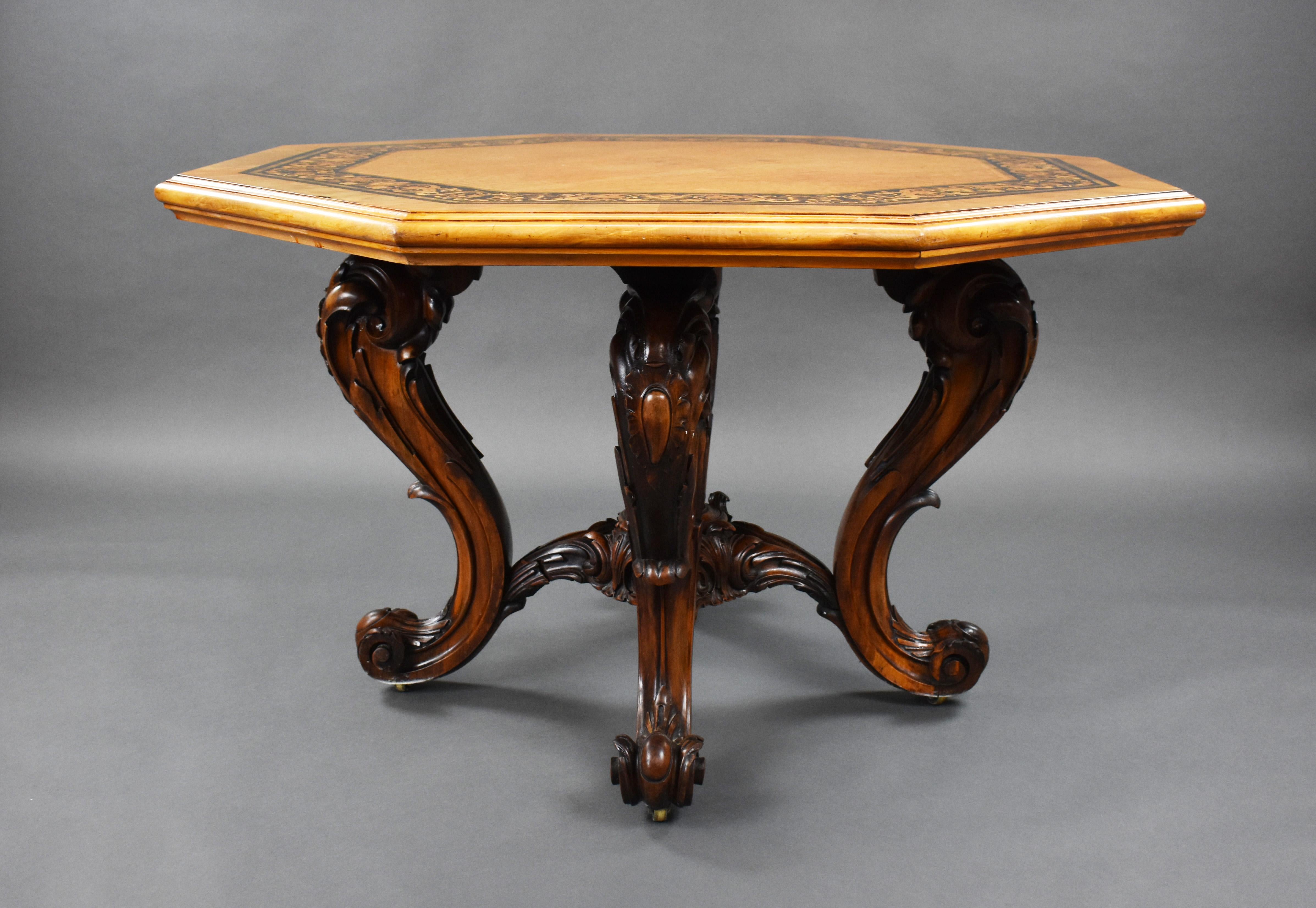 A good quality Victorian burr walnut center table, having a marquetry inlaid top, above ornately carved walnut legs united by a central stretcher with carved center motif, raised on brass castors. The table remains in good, untouched