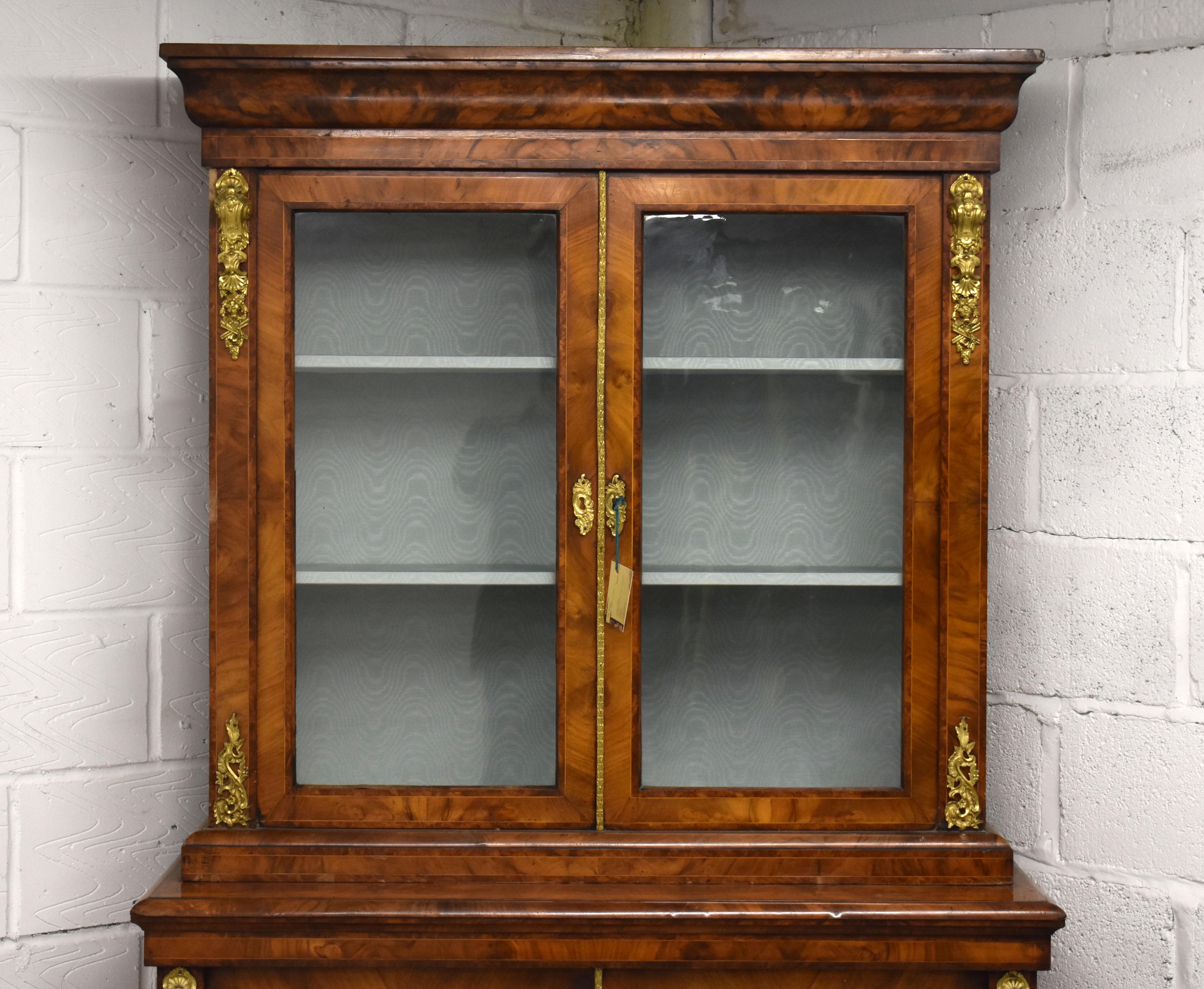 Selling is a superb quality Victorian burr walnut bookcase. The bookcase is banded in various woods. The top of the bookcase has ormolu mounts on each corner and glazed doors and sides and encloses two shelves, and has ormolu beading to the edge of