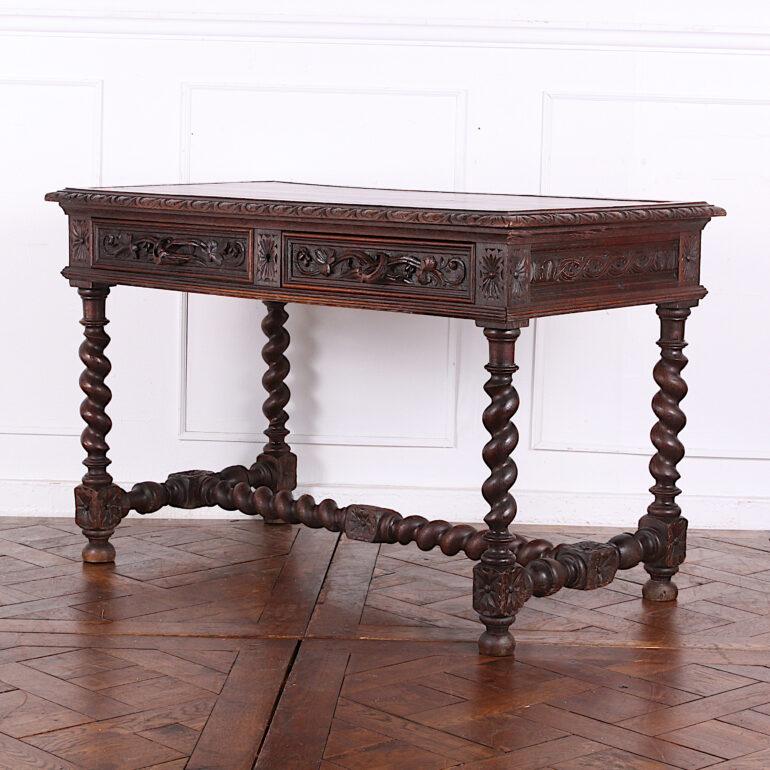 Highly carved oak barley twist desk from England, the two frieze drawers with carved 'branch' motif handles, the top with carved edge and inset gilt tooled leather writing surface, the whole standing on spiral-turned legs and 'H' stretcher. In
