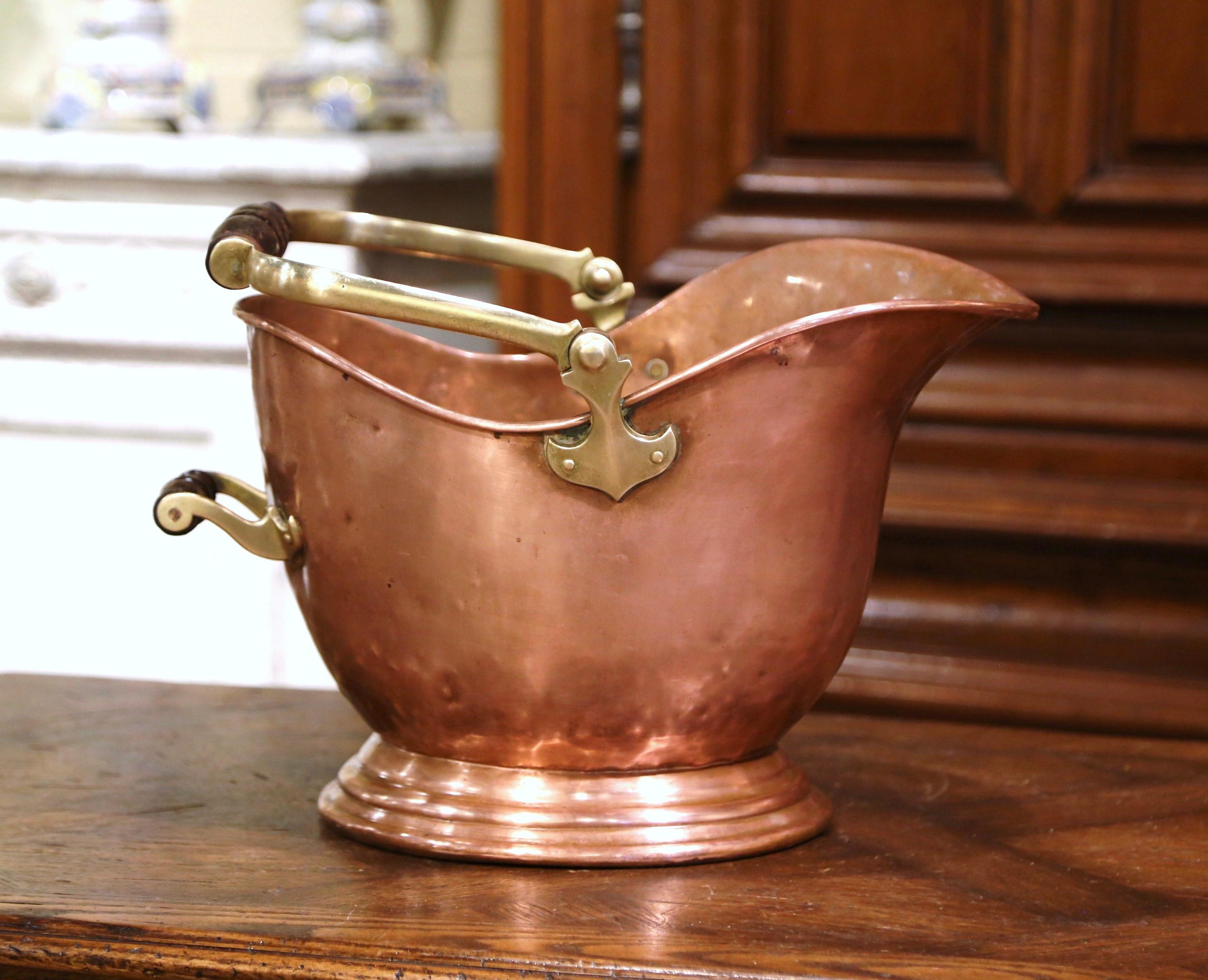 This antique coal scuttle was created in England, circa 1880. Built of copper with a brass and turned walnut handle, the oblong bucket stands on a round base. The versatile decorative box is in excellent condition; it could be use next to a