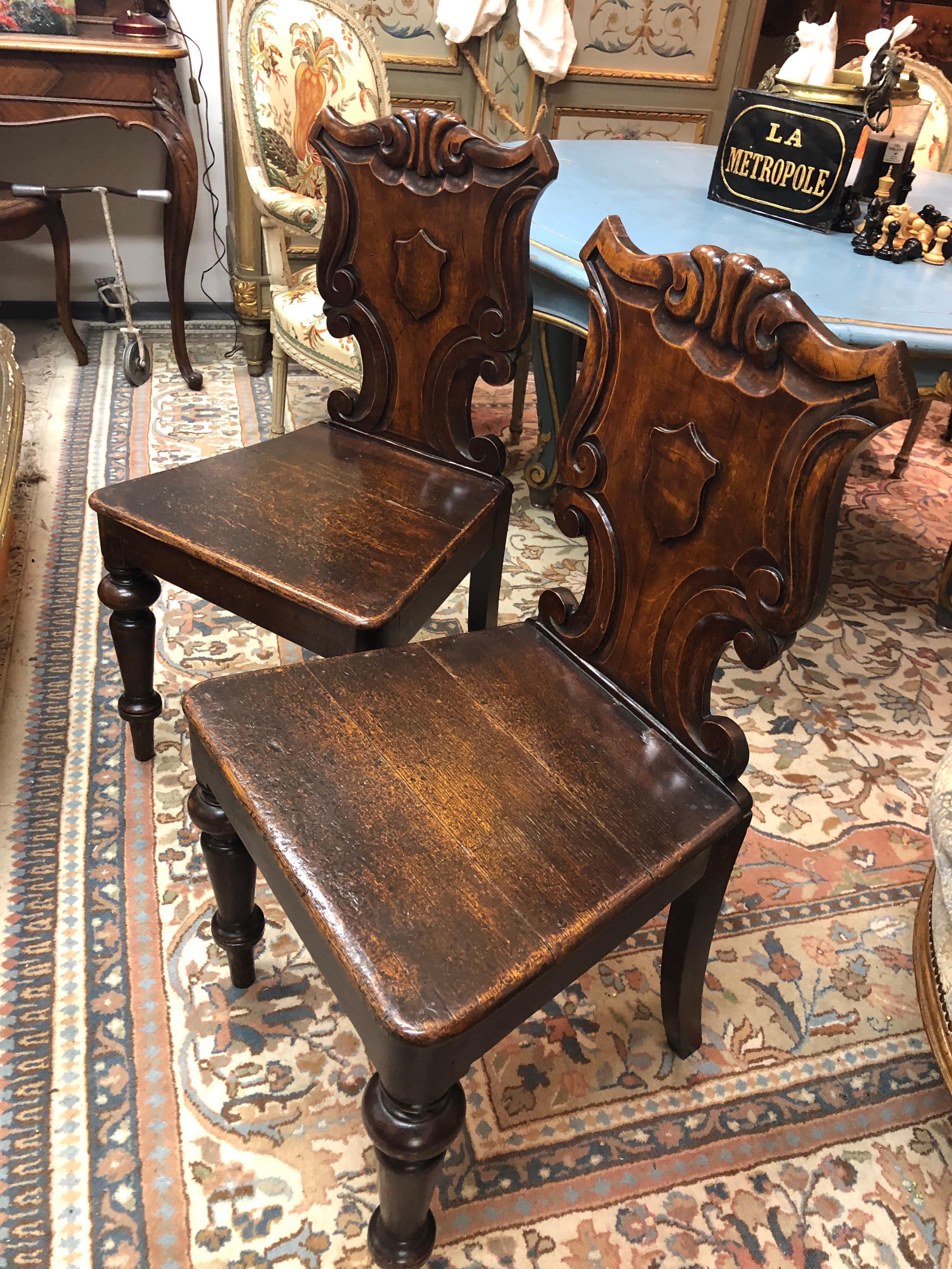 A pair of Victorian oak hall chairs, each with a scroll carved back, centred with a vacant shield, on turned front legs.
England, circa 1860
From the private collection of Sir J. Lever.