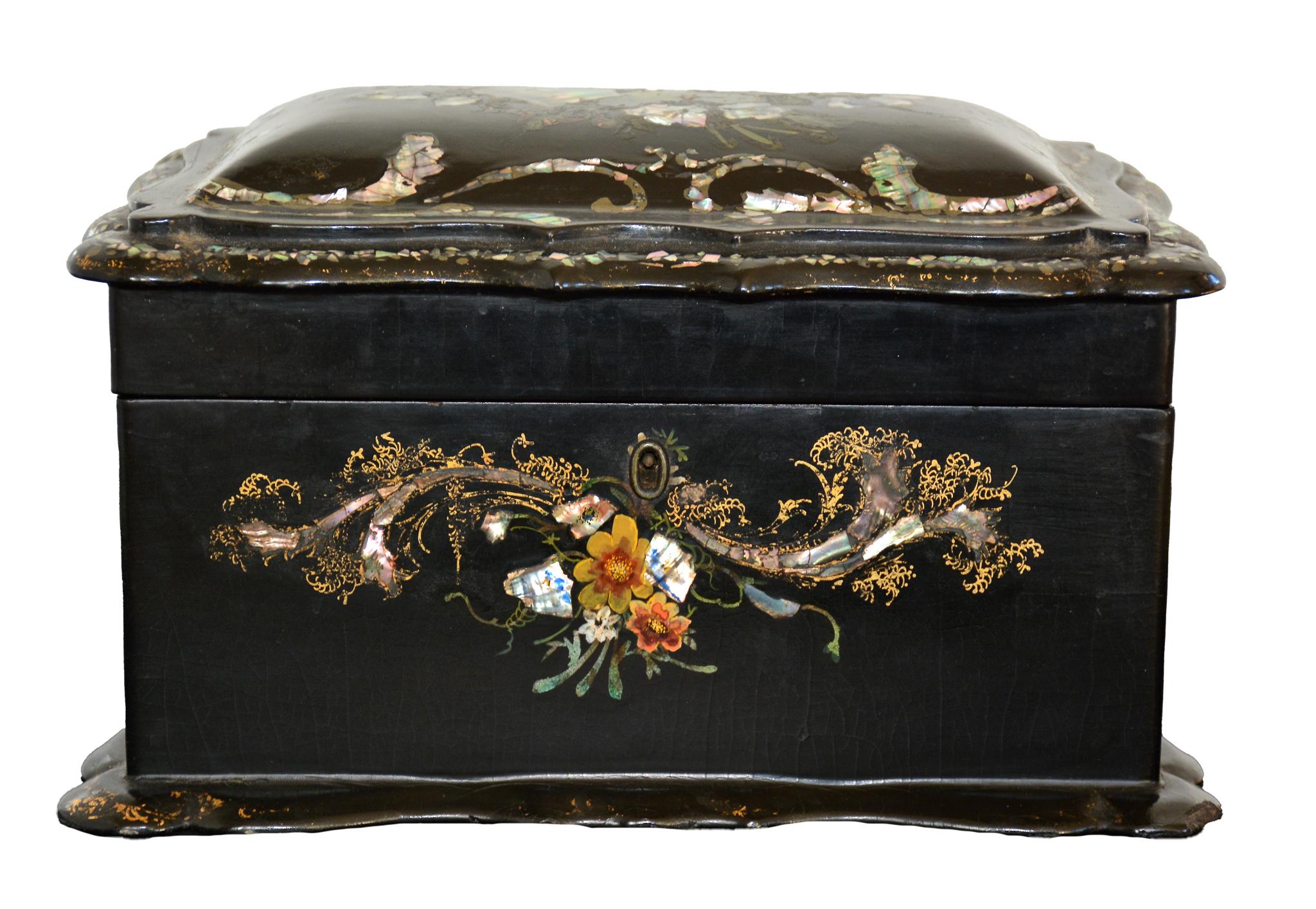
This exquisite Papier Mâché box, circa 1870s, has a black lacquered finish with mother of pearl inlays,  gold leaf hand-painted floral motifs and embellished decoration. 

The English Victorian box is dressed with a scalloped apron surround base,