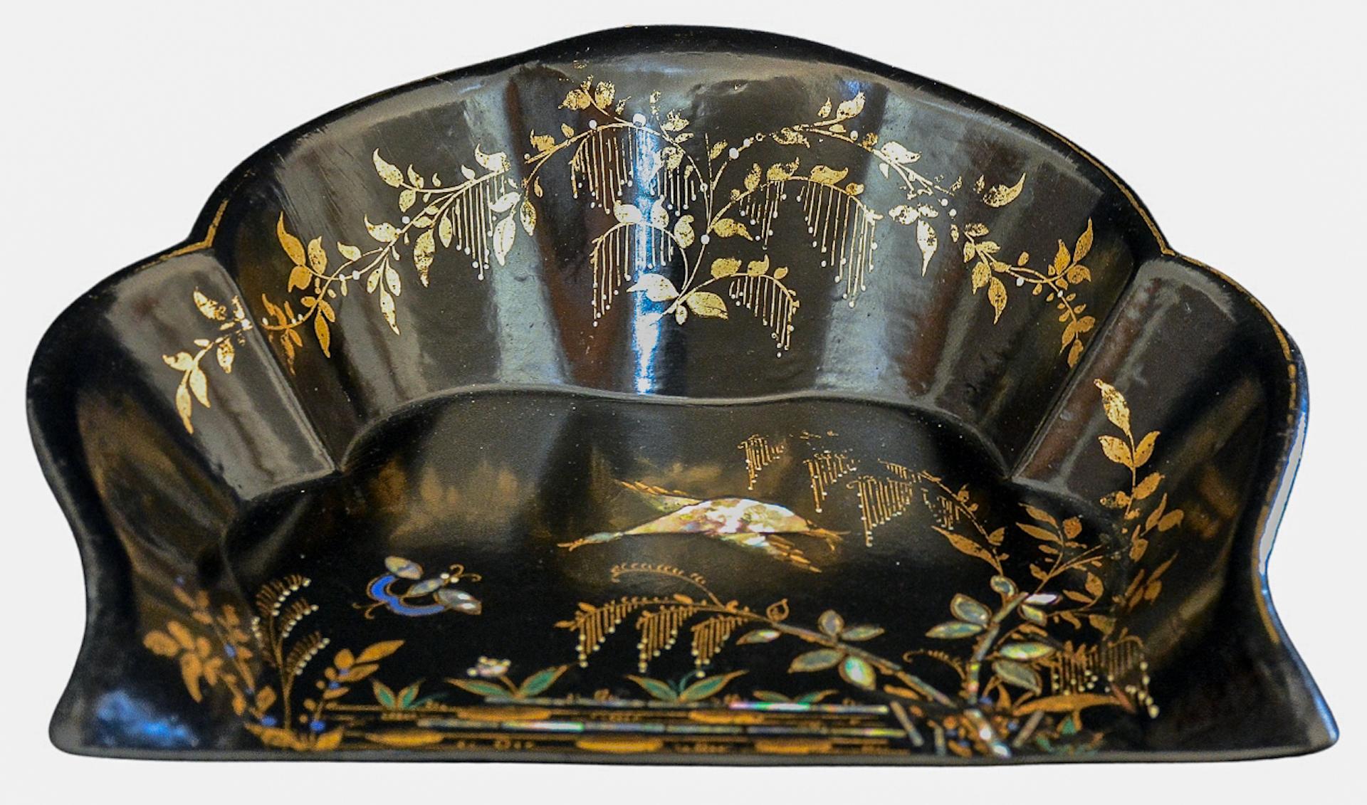 Este exquisito recogedor de polvo de papel maché con incrustaciones y pan de oro, de hacia la década de 1870, tiene un acabado lacado en negro con incrustaciones de nácar,  Diseño floral pintado a mano en pan de oro y escena ribereña con