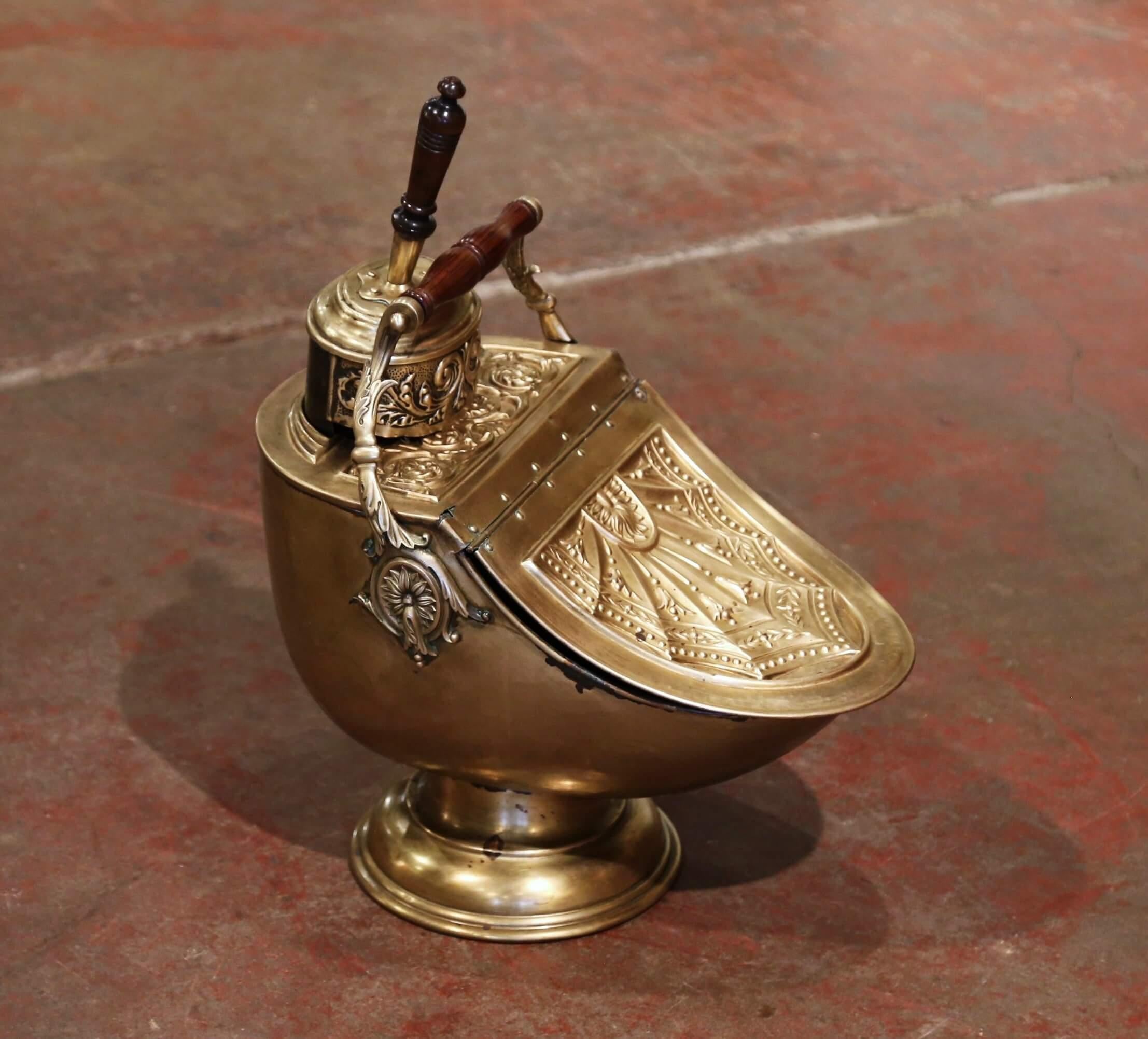This antique coal scuttle was created in England, circa 1880. Built of brass with foliage repousse decor, the patinated bucket stands on a round base and features a large turned walnut handle at the pediment, the original brass scoop with wooden