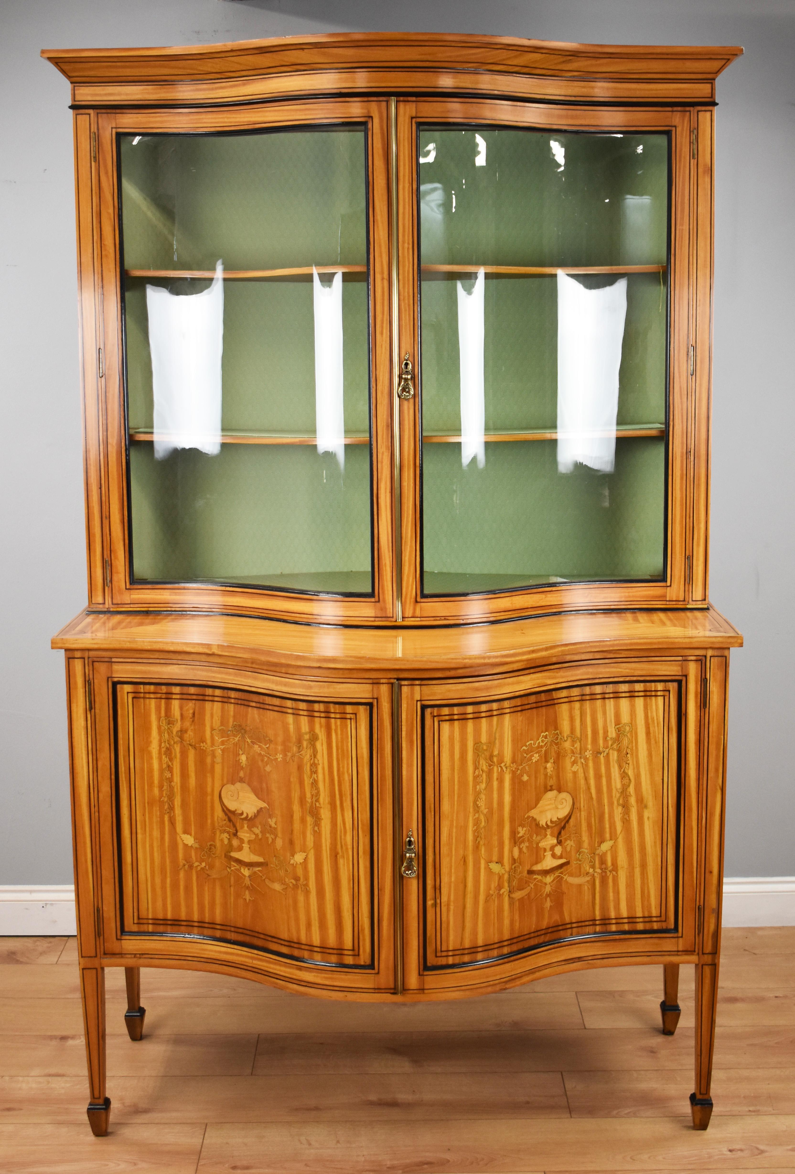 For sale is a fine 19th century satinwood serpentine display cabinet, inlaid with ebony stringing and edged with ebonized moulding, the upper section has a moulded cornice above to glazed doors opening to shelves. The base section, with well swept
