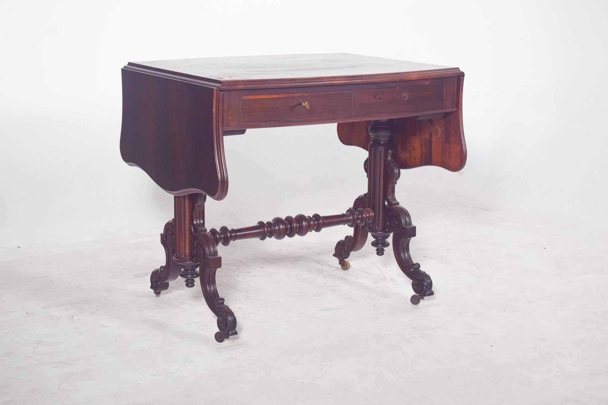 Victorian Tabled Table in rosewood, with Two Drawers. The top features two cut-out movable side flaps which, when raised, extend the top, revealing the functionality designed to optimise space without sacrificing elegance.
The highlight of the piece