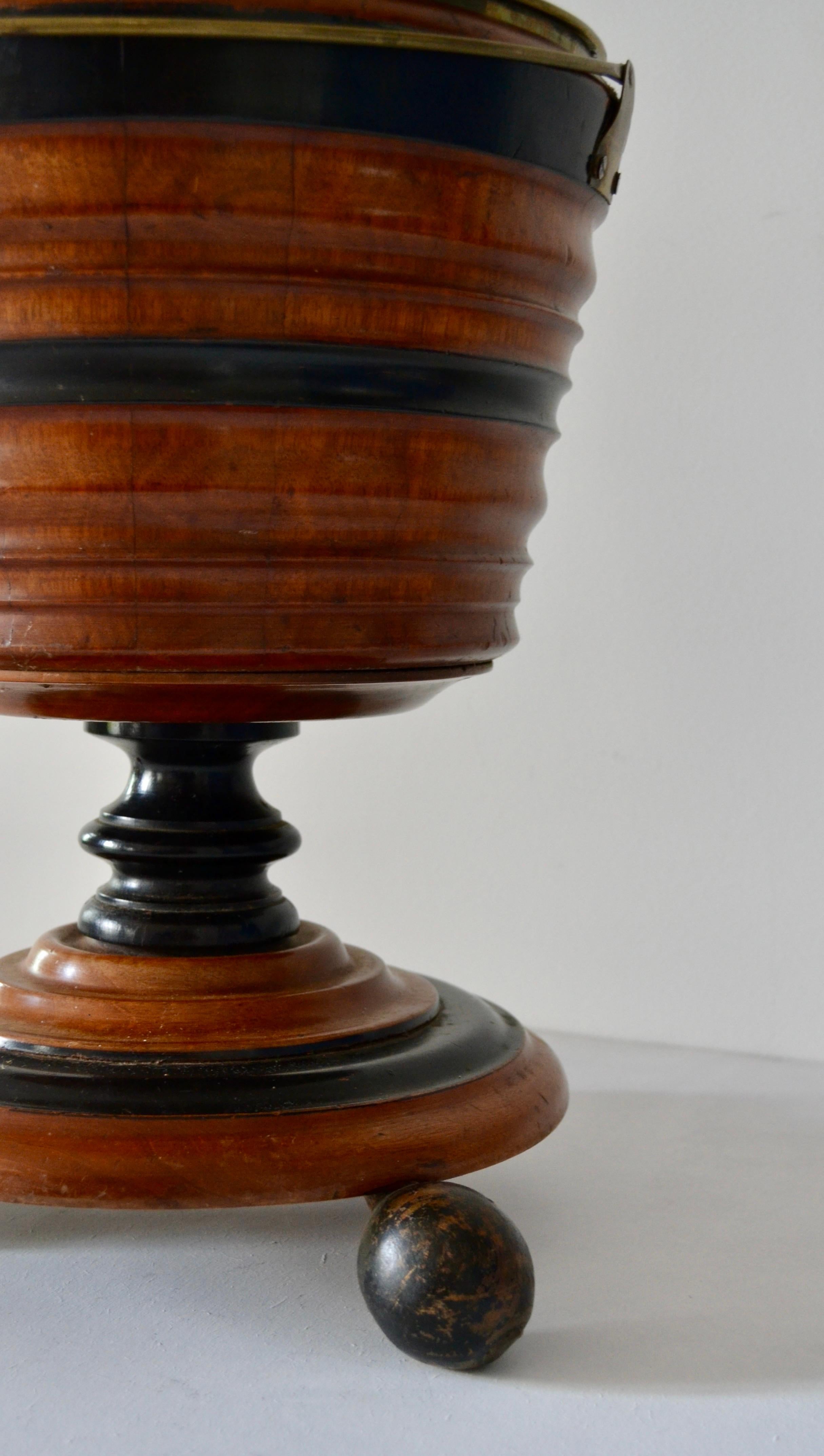 An English walnut and ebonized wood peat (or coal) bucket, circa 1860–1870, resting on three ball feet.
These buckets were commonly used in England and Ireland during the 19th century to transport peat for fuel, though they could also serve for