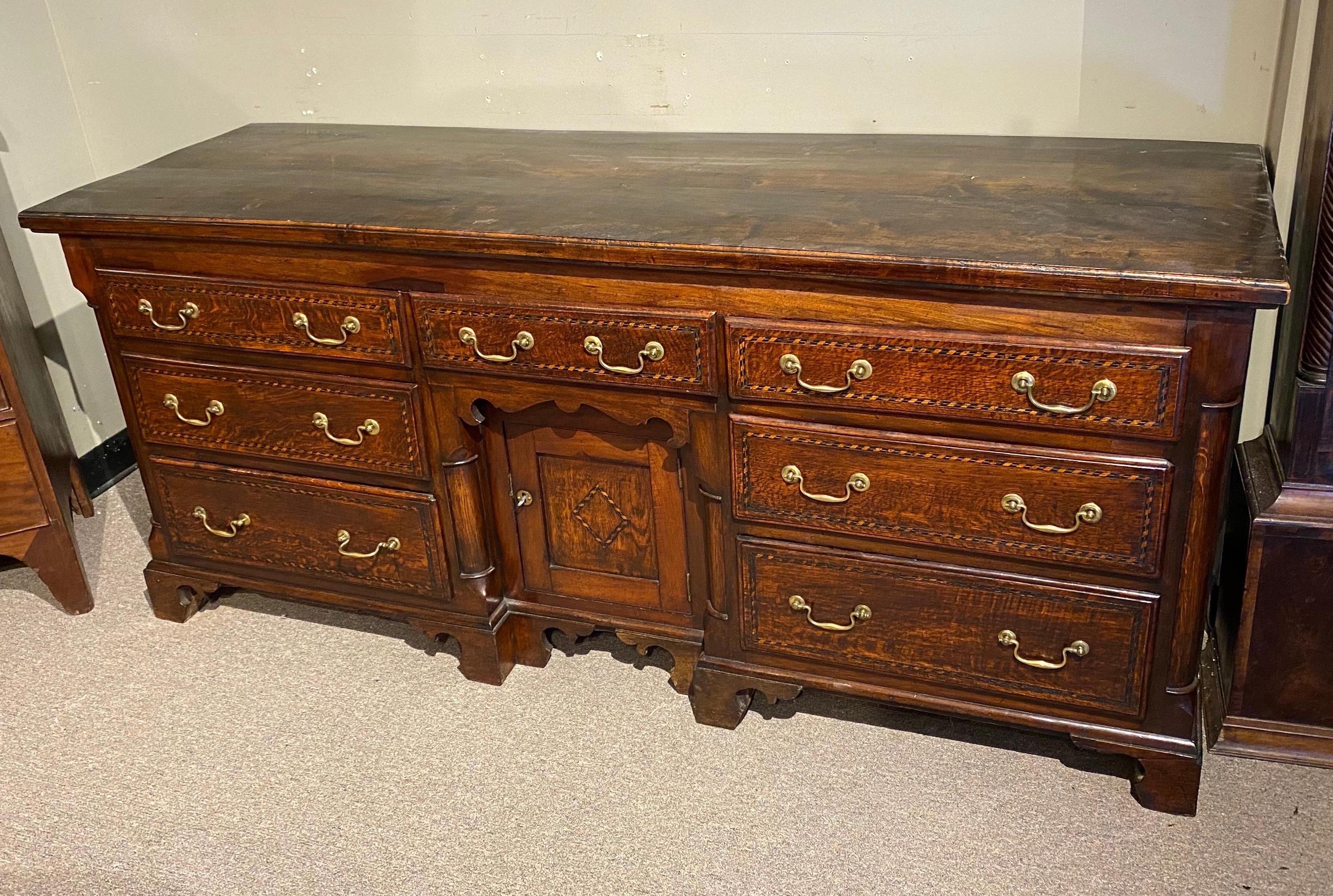 19th century English walnut and oak dresser base on bracket feet with 7 drawers and open cabinet space behind prospect door. Drawer fronts all inlaid. Carved quarter columns. Charming piece with nice old, mellow color.
