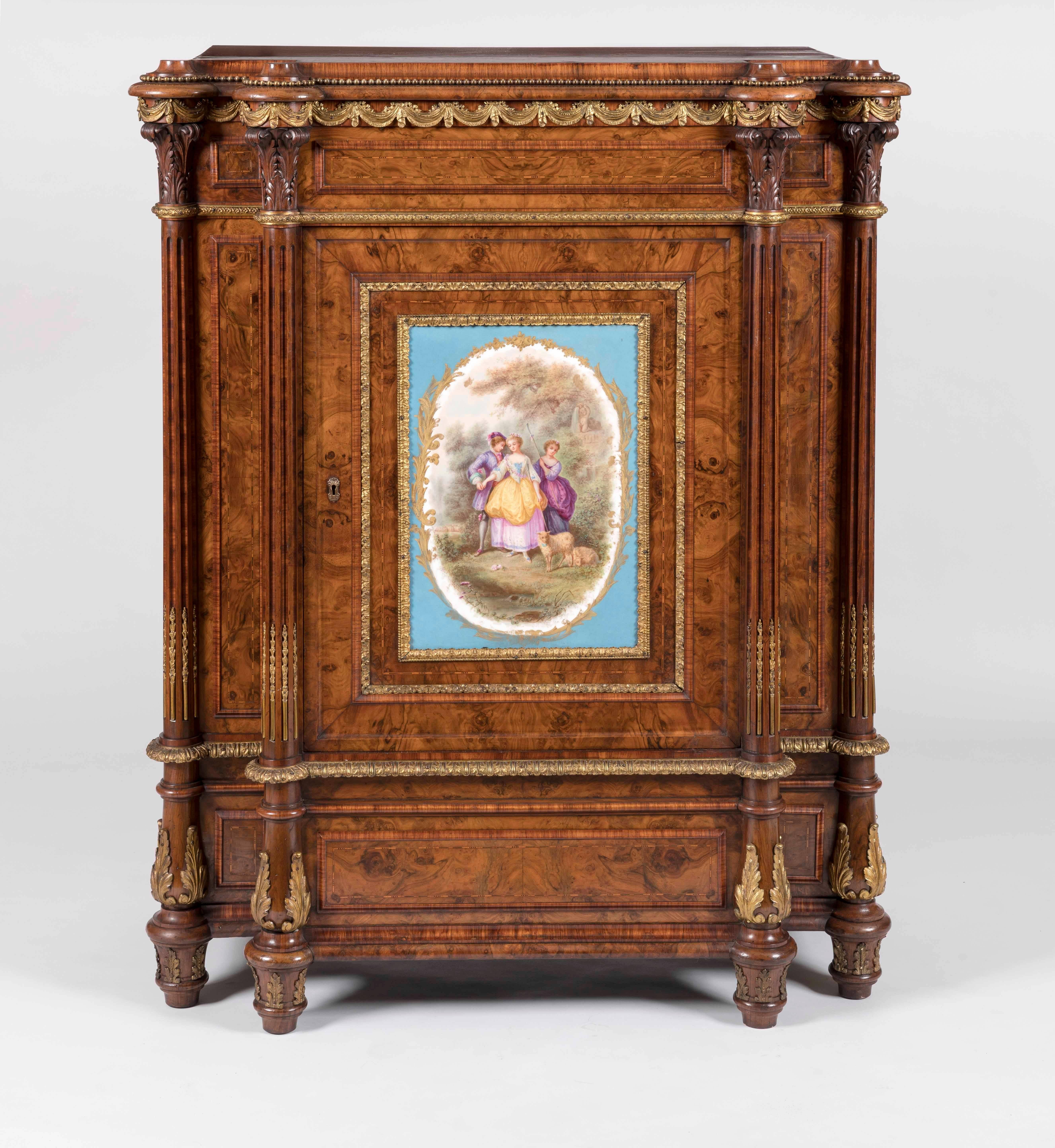 A drawing room cabinet

Constructed in Circassian walnut, exuberantly dressed with gilt bronze mounts and a central situated oblong 'Sevres' plaque; rising from an inverted serpentine plinth base, four fluted columns flanking the centrally