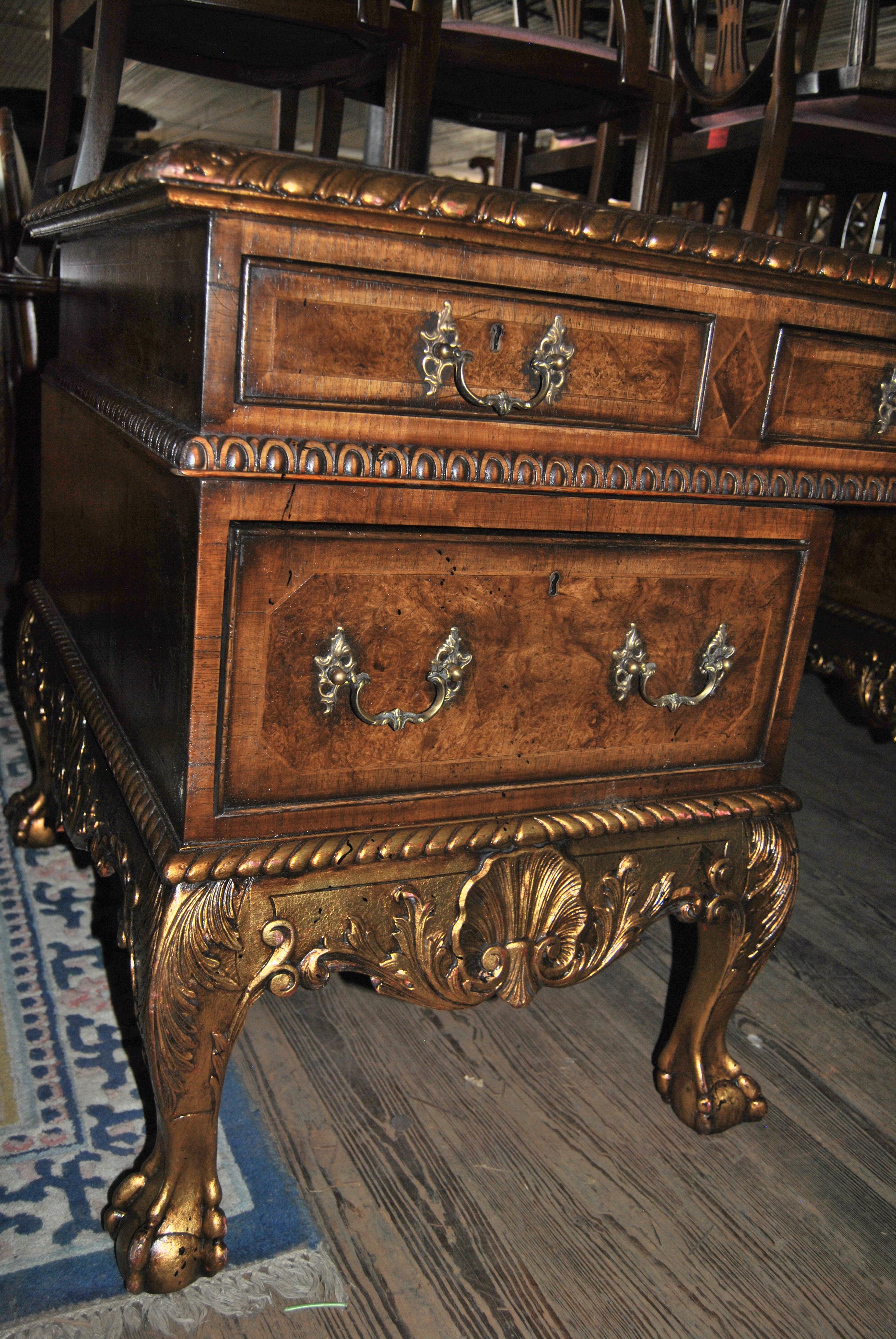 This is a walnut desk made in England, circa 1840. The top has a nicely shaped green leather writing surface with gold tooling. There is a hand carved gadrooned edge around the entire top that is done in a gold gilt. There are 4 drawers across the