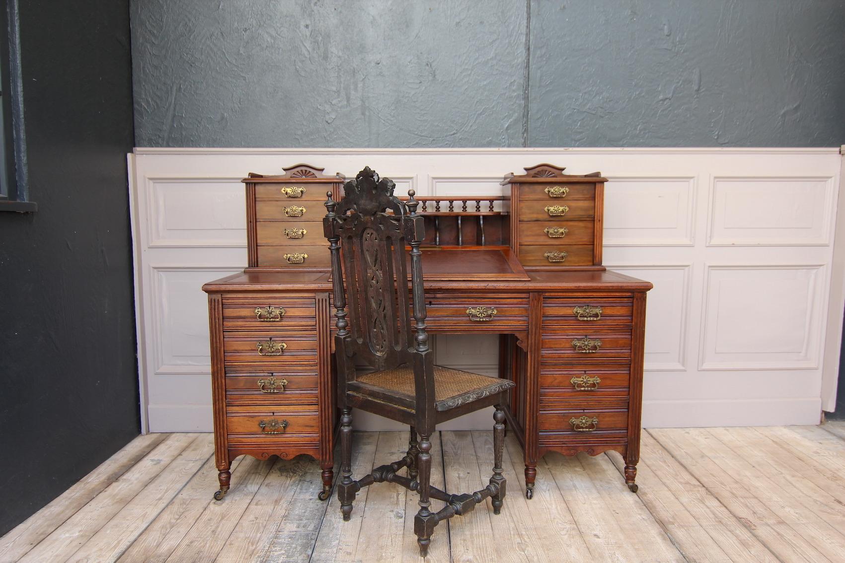 A late 19th century English writing desk. Made from solid walnut.

High-quality desk standing on eight swivel castors with a total of 16 lockable drawers and a desk flap. The small drawers of the attachment can be closed with the fluted strips