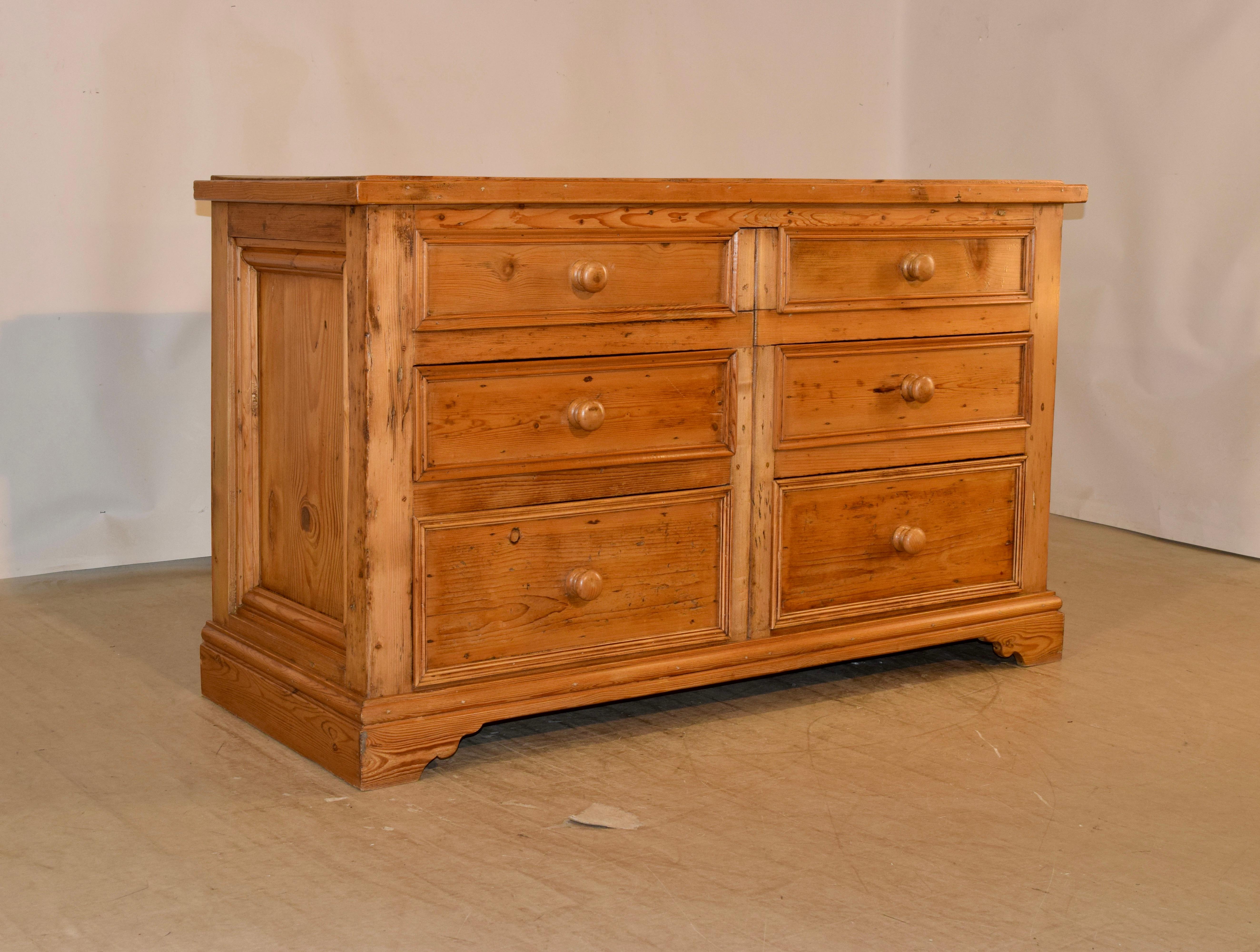 19th century English wide chest of drawers made from pine. the top has a molded edge, following down to hand paneled sides and six drawers in the front. The drawers are paneled as well, and the case is raised on bracket feet in the front and a