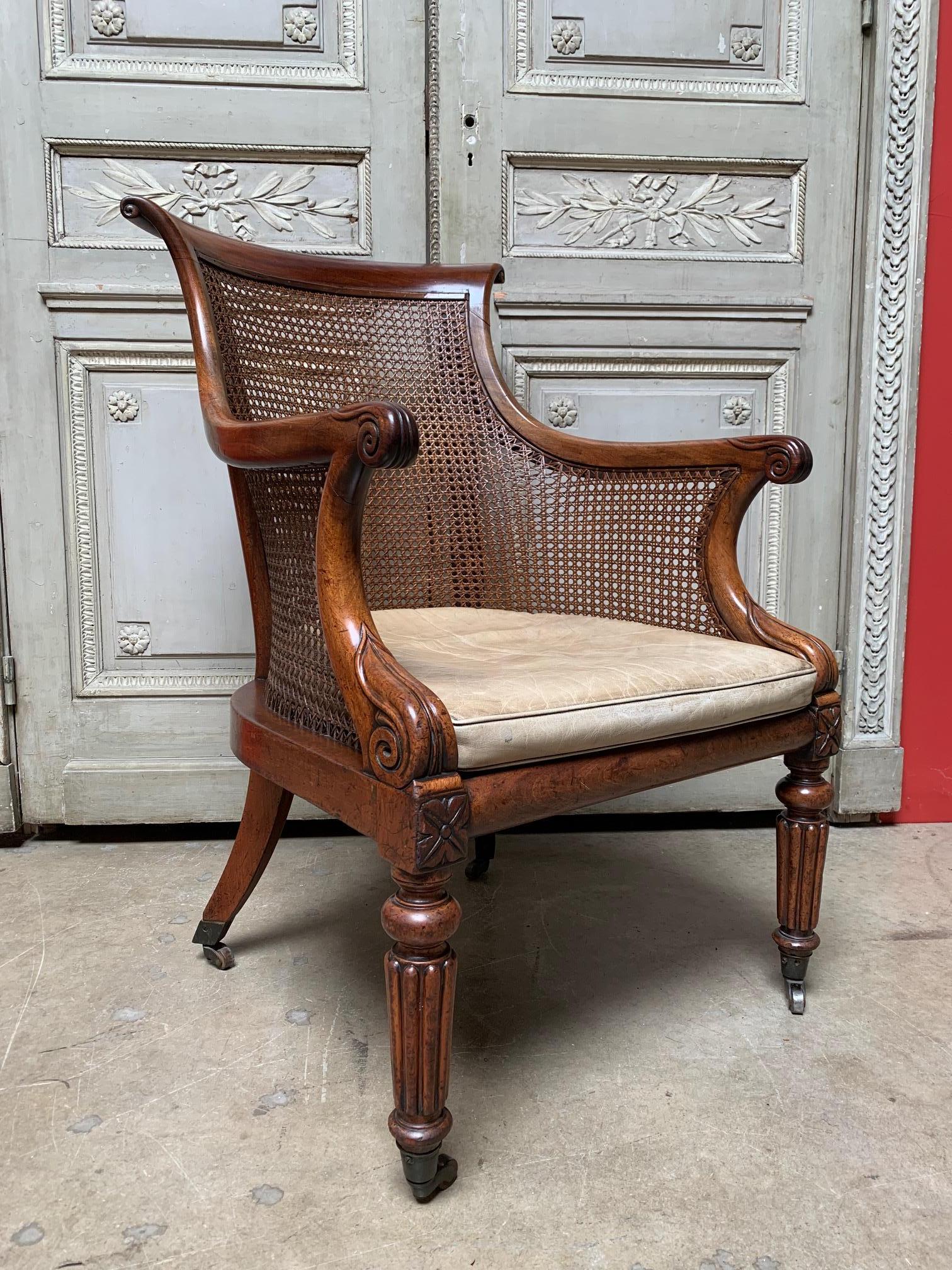 English William IV carved walnut and cane library armchair with brass casters and a taupe leather seat cushion. This armchair has a wonderful patina and the cane is in good condition. The leather cushion is old but still usable.