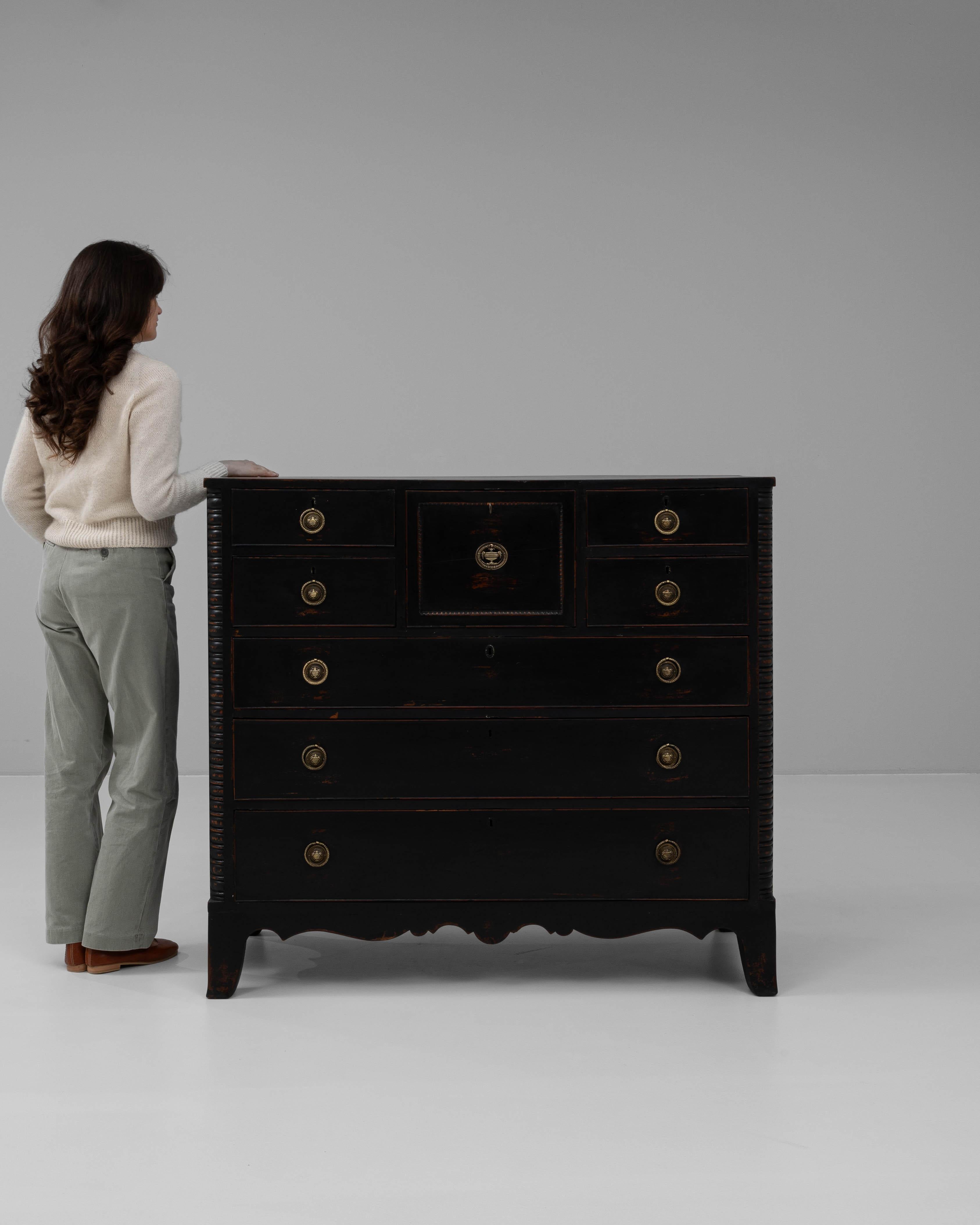 This 19th-century English black patinated chest of drawers showcases a sophisticated design with an elegant distressed finish that adds timeless charm. Crafted from solid wood, it features a striking black patina with subtle wear that enhances its
