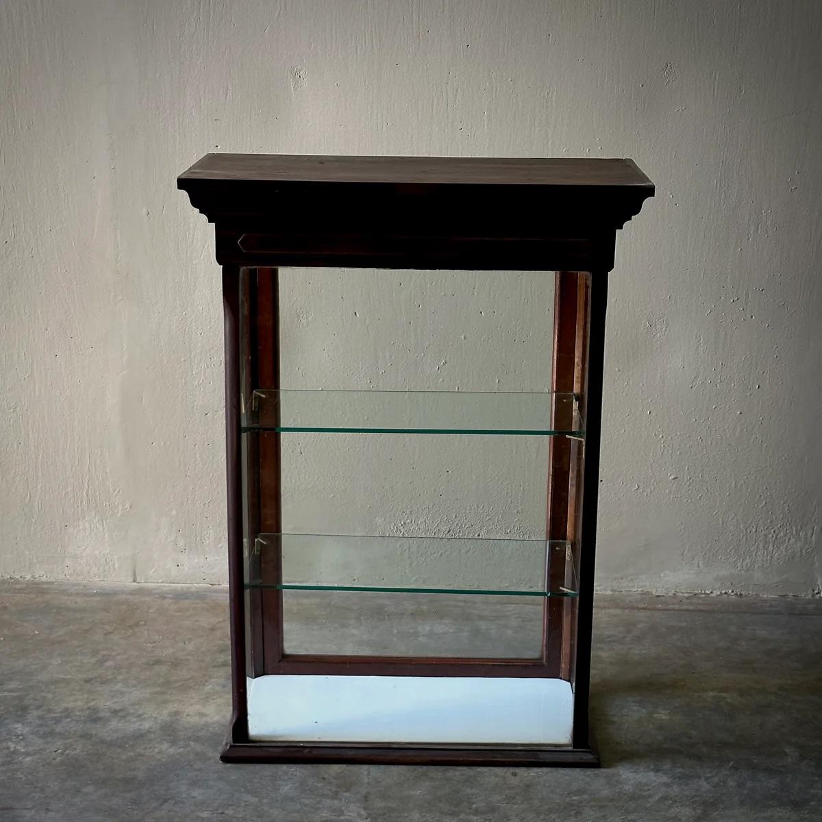This Victorian tabletop display case blends utility with aesthetic appeal through its elegant cherry-toned wooden framework and beveled cornice, providing an architectural flair. Glass walls and shelves allow for 360-degree visibility, making it an