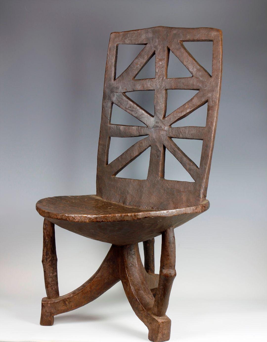This large, impressive nineteenth-century Ethiopian throne, from the Wollega Oromo culture, features a high, upright back-rest. 

An attractive cut-out cross formation, typically found among chairs from this region of Ethiopia, decorates the back
