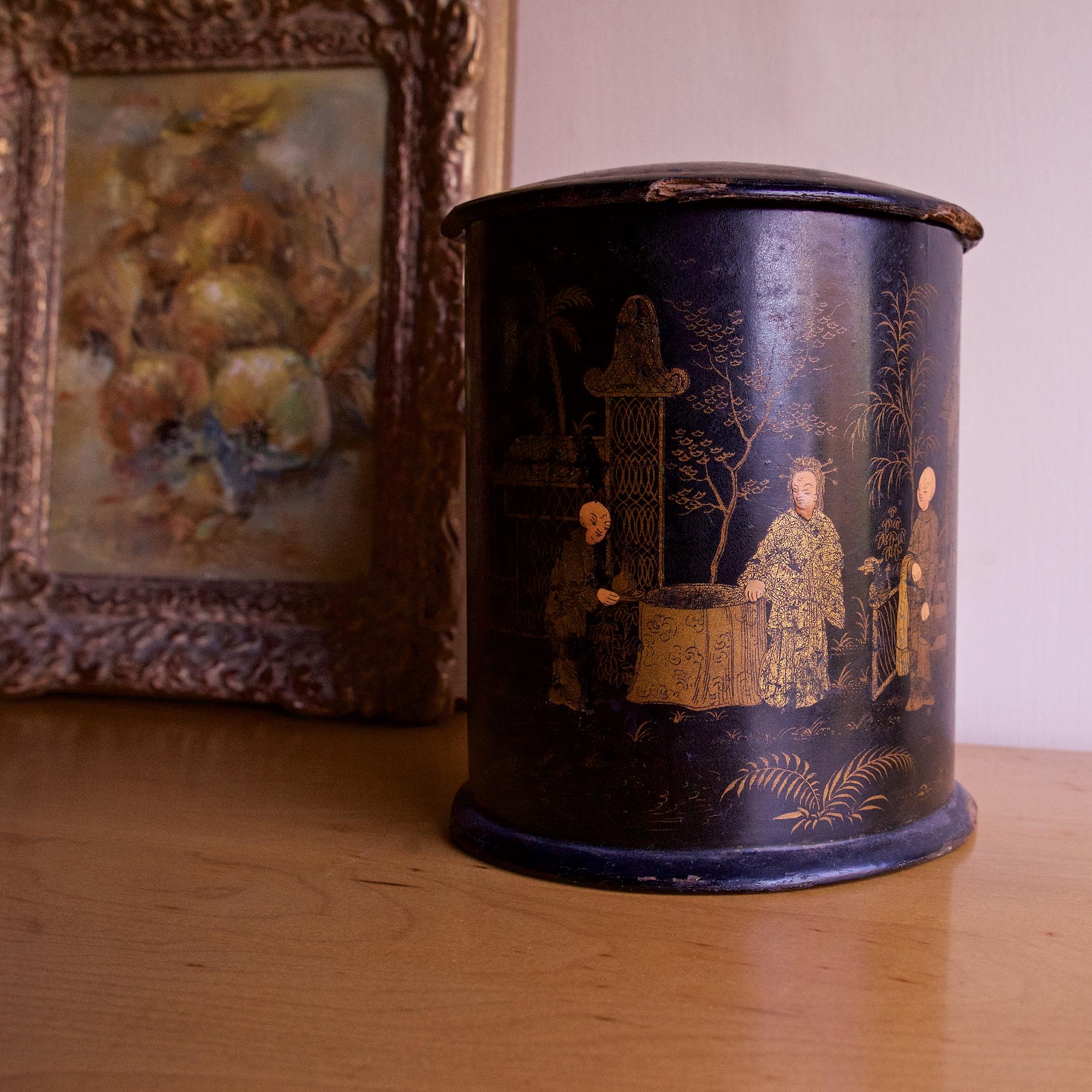 A large English lacquered papier-mâché container from the Aesthetic Movement period, featuring a decorative chinoserie painting of stylized Asian figures, pagodas, and a garden bridge.  Silver foil lined interior, and floating inner lid.  6 inches