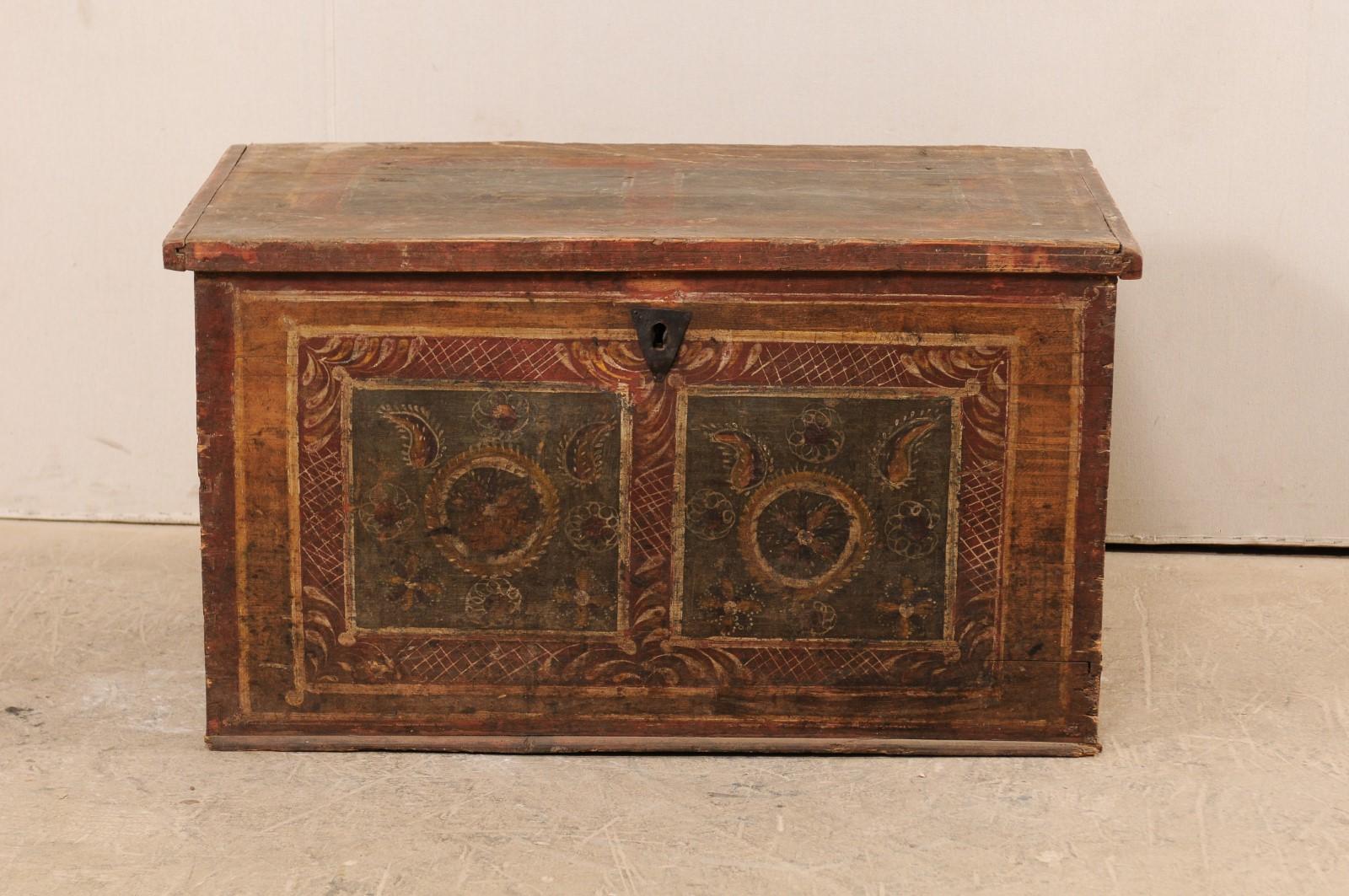 A European storage chest from the 19th century. This antique trunk, with it's rectangular-shaped body, features it's original hand painted decorations about the top front sides in a paisley and foliage motif within framed squares, and it's original