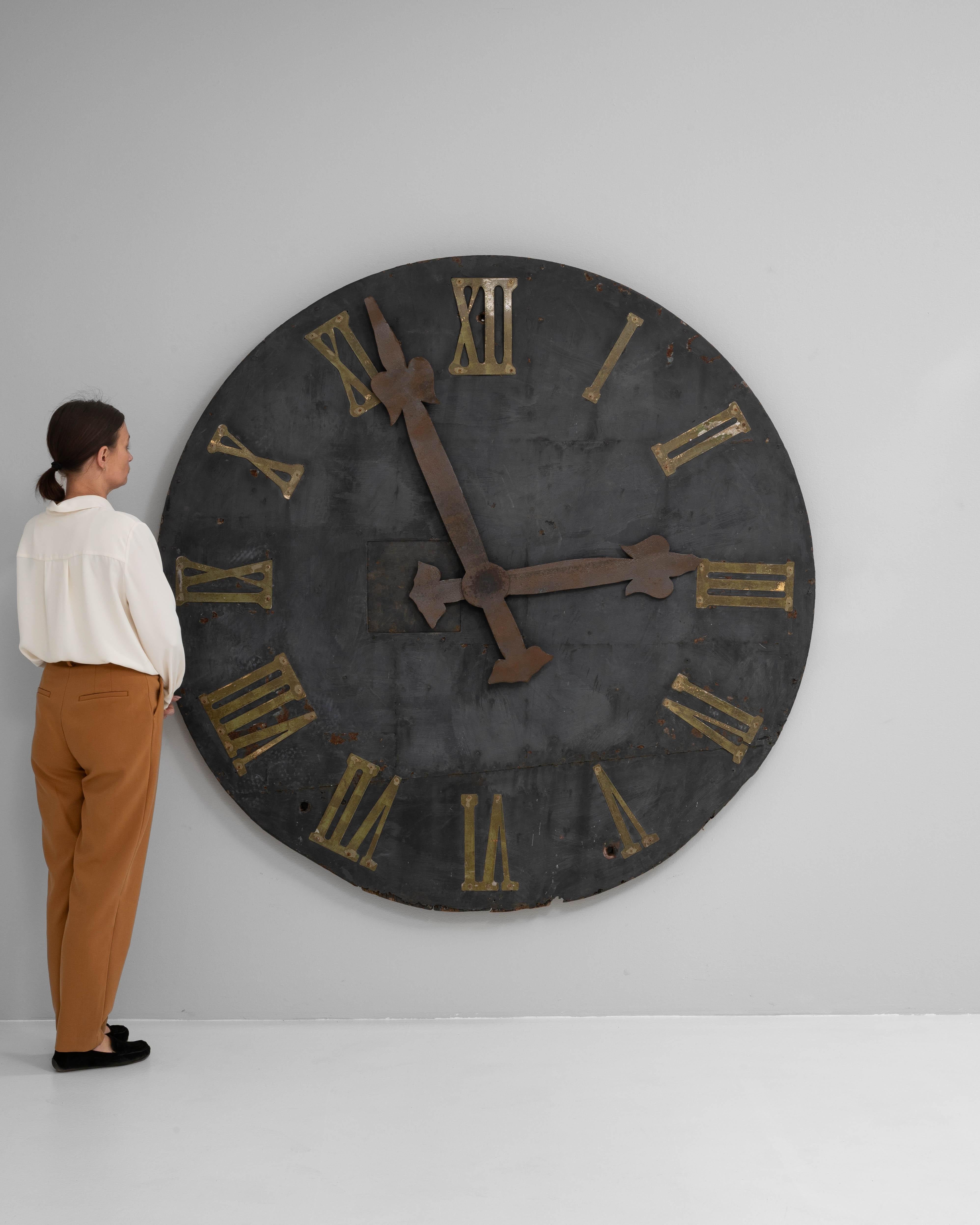 This 19th Century European industrial wall clock face is a commanding relic of utilitarian architecture, likely salvaged from a train station, public building, or factory. Constructed from heavy metal, the surface bears a deep, timeworn patina with