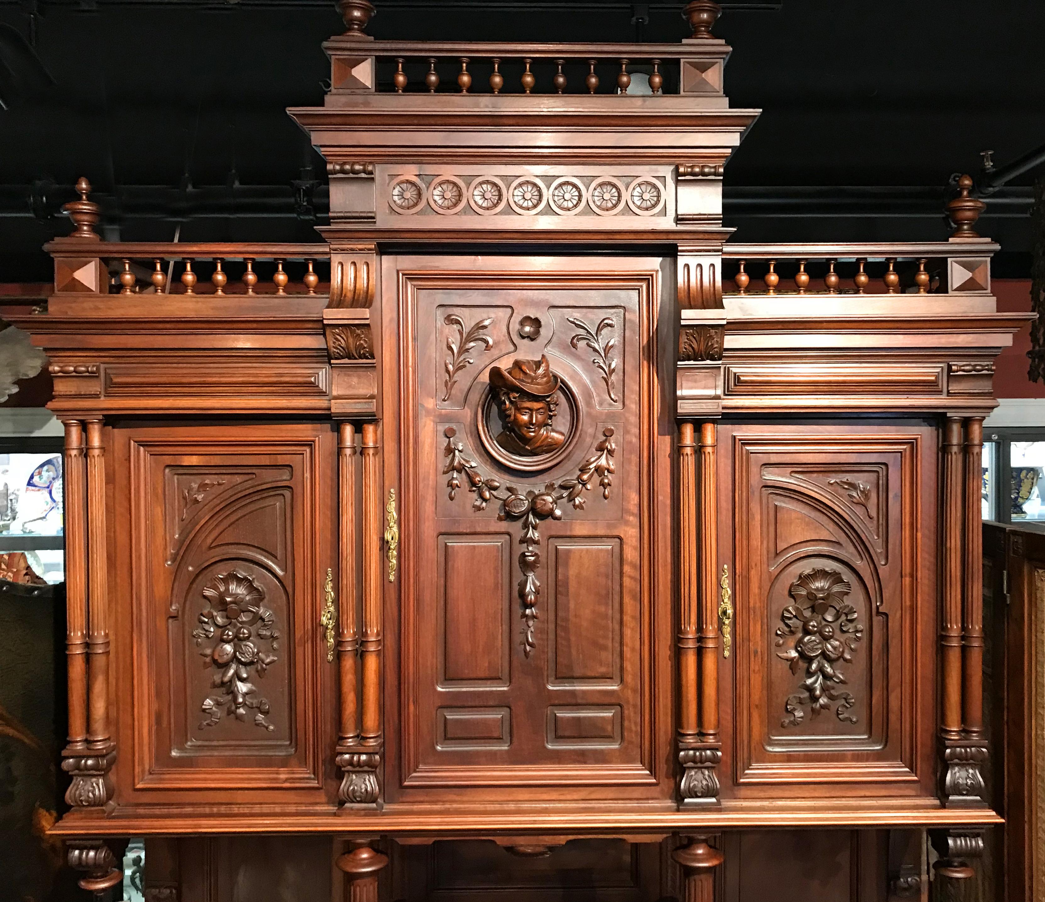 An exceptional two part court or castle cupboard or server in walnut, the upper case with upper spindle gallery featuring corner turned finials surmounting three large doors, each ornamented in high relief with a female figure on the center door,