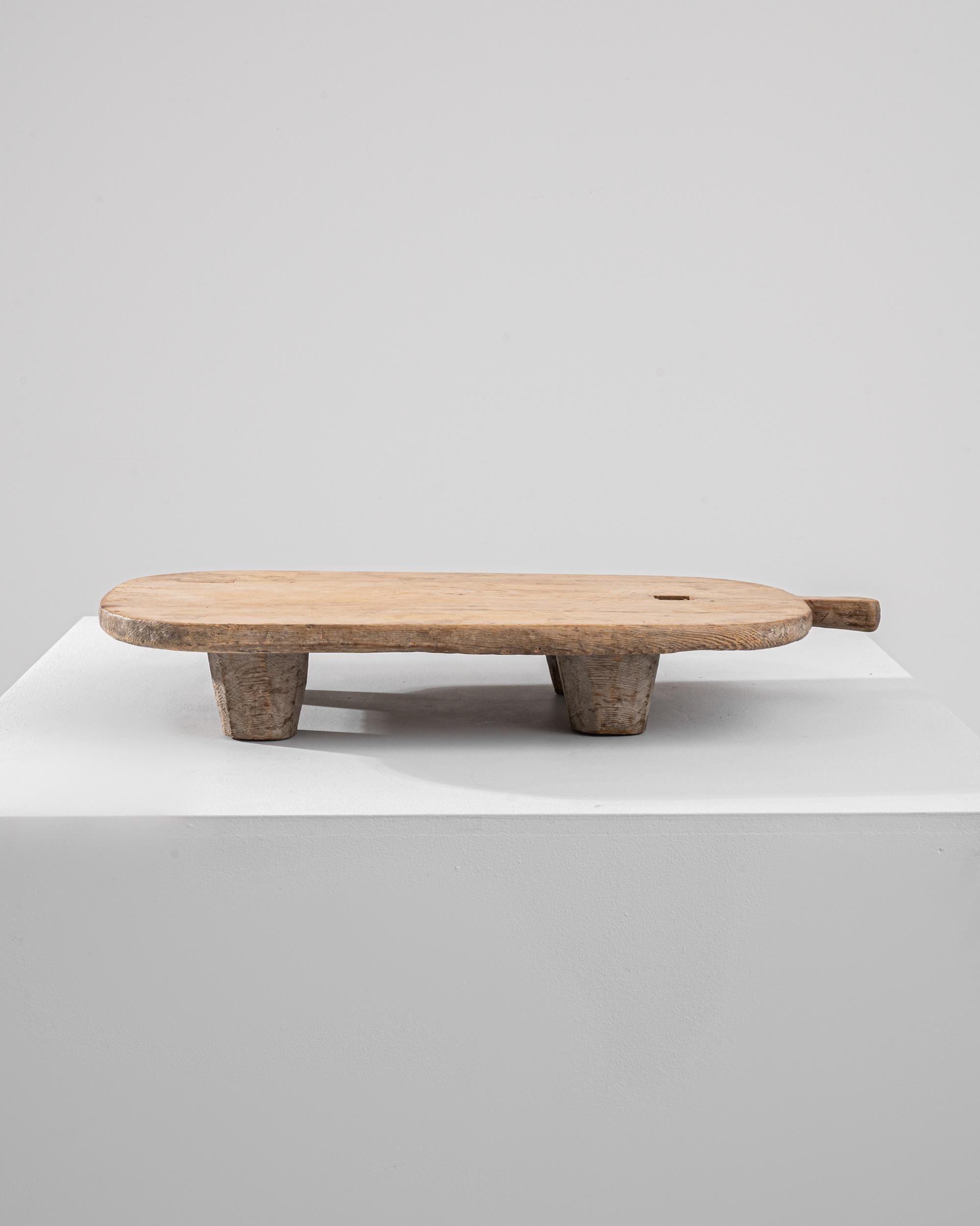 A wooden tray made in Europe during the 19th century. This unassuming and gently shaped cutting board emits a familiar and comforting demeanor. Made from a simple slab of wood, buttressed by short tapering legs, one is able to consider the tree it