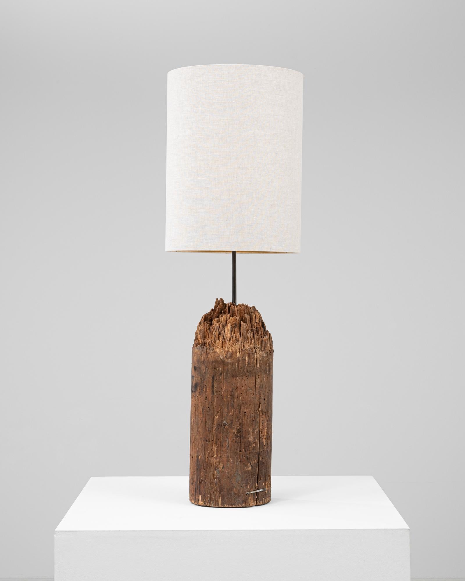 Questa lampada da tavolo europea del XIX secolo è caratterizzata da una base di grande effetto realizzata con un frammento di legno invecchiato naturalmente, conservato nel suo stato grezzo e consumato dal tempo. La forma cilindrica conserva il