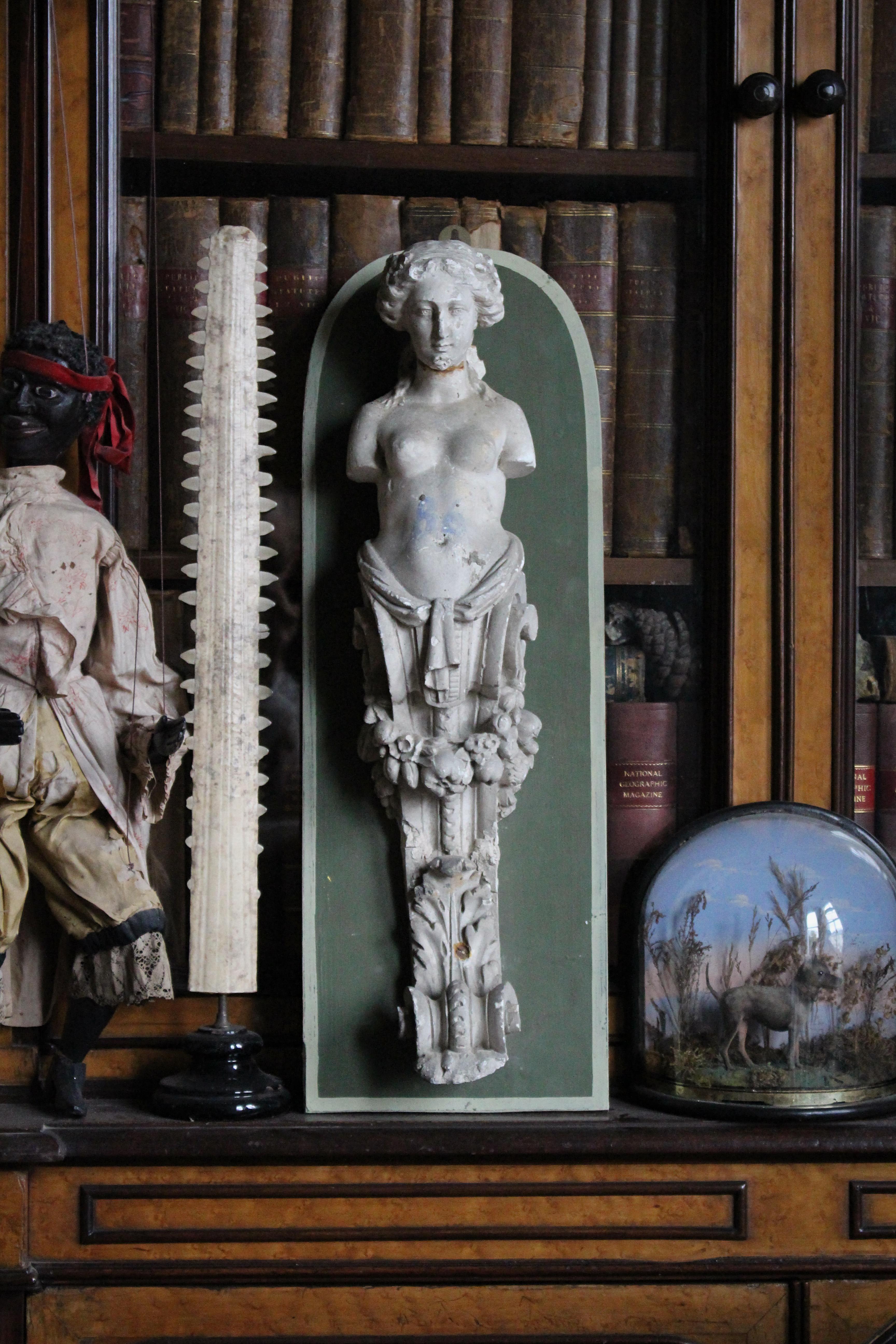 A well cast plaster corbel, of a classical female figure. Likely an ex museum piece or a foundry sample, with an inventory number of 186.

Later mounted on decorative green painted hanging board.

Age related knocks and abrasions, rust residue and