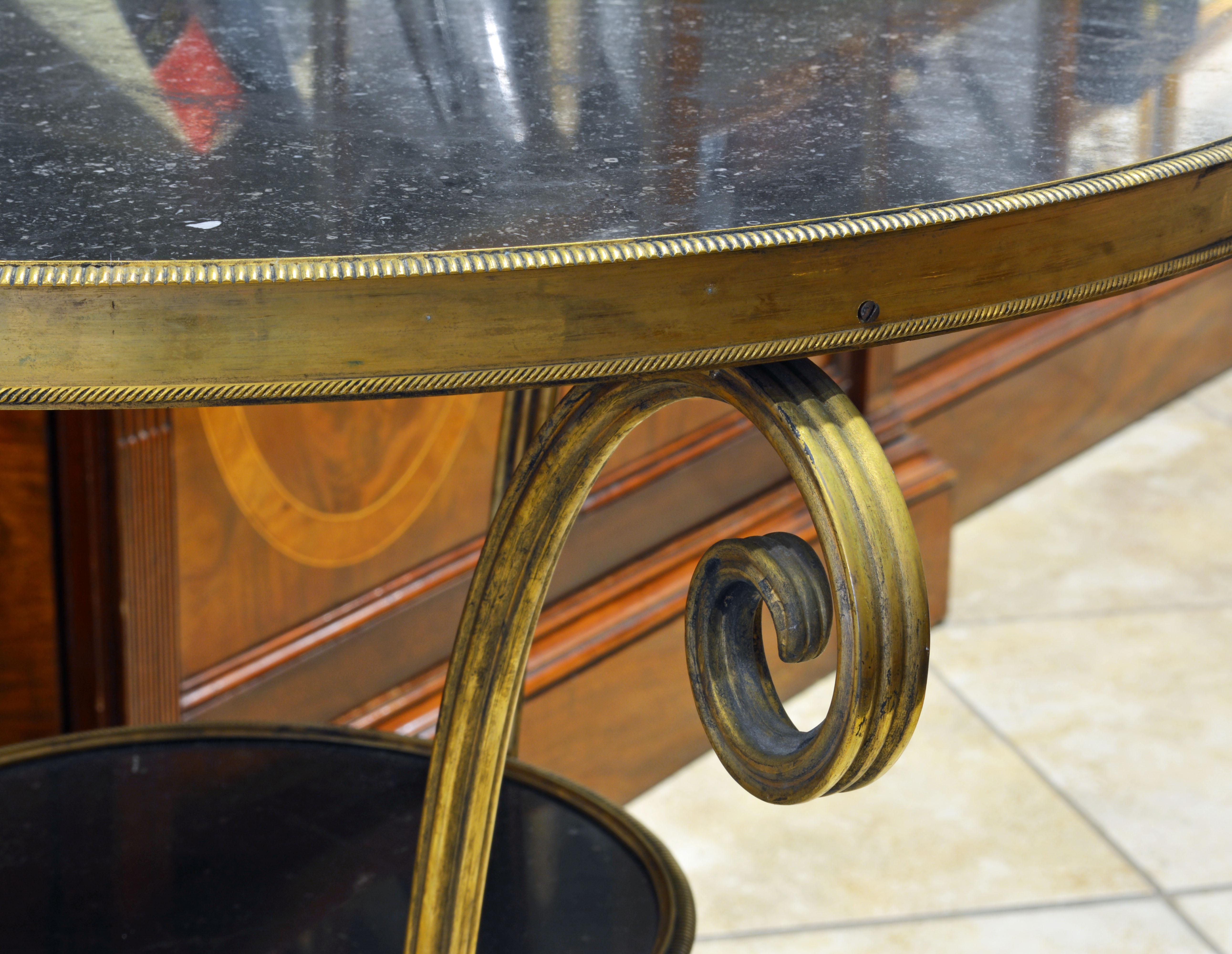 This French Empire gueridon table of the period features a black marble top beautifully edged by an ornate bronze gallery resting on three elegantly curved legs ending in paw feet with casters and united first by a second tier bronze edged marble