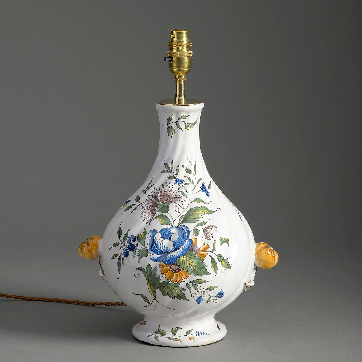 A late nineteenth century Faience pottery swirl form vase, decorated with polychrome glazed flowers upon a white ground with flower head knop handles to the sides. Now mounted as a table lamp.

Dimensions refer to pottery vase only.

Wired to UK