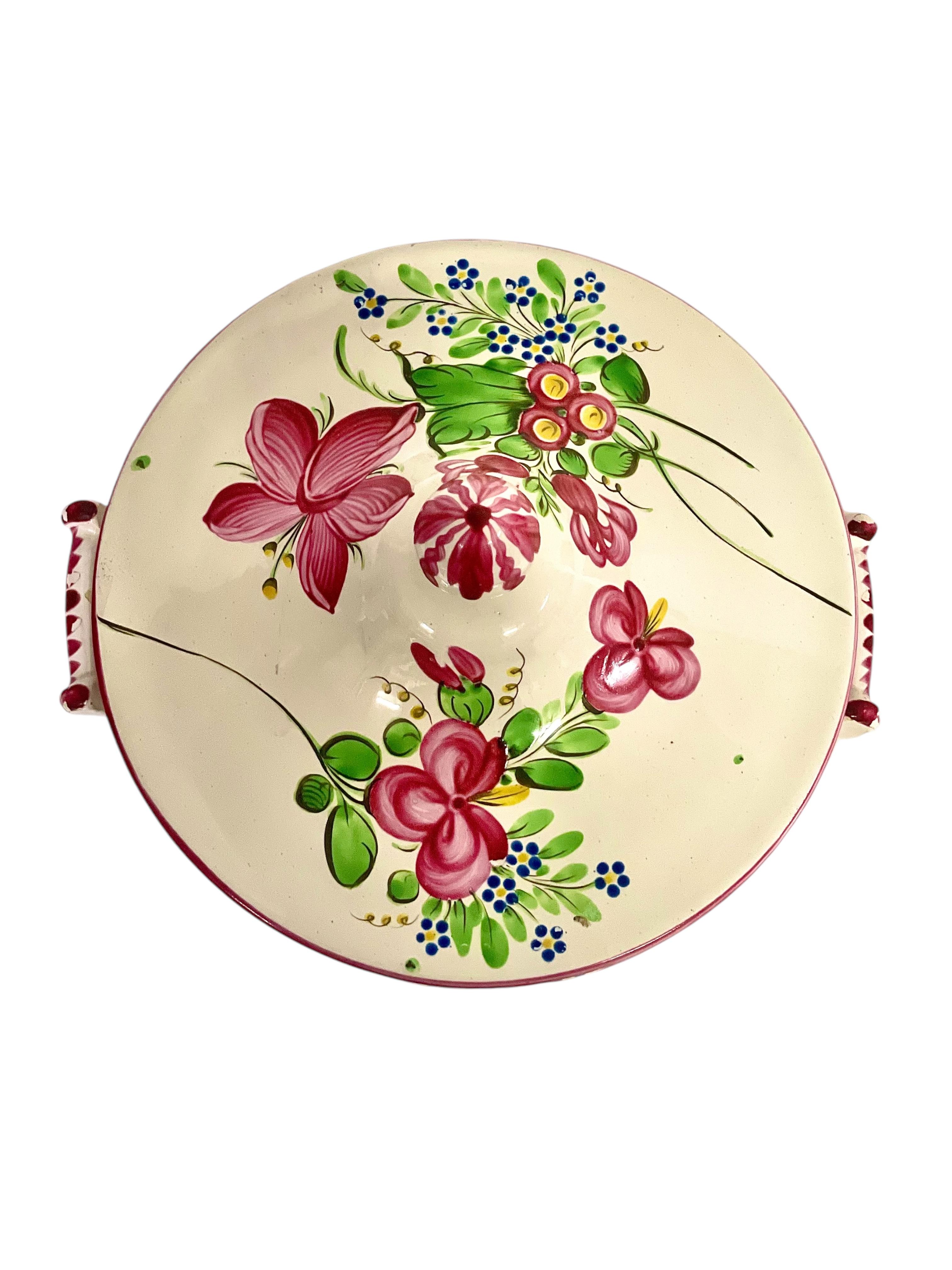Questa incantevole zuppiera francese è un delizioso esempio di ceramica faience tradizionale dipinta a mano, che ricorda la produzione di Keller & Guérin presso la manifattura di Lunéville. Conosciuta per le sue stoviglie colorate e allegre alla