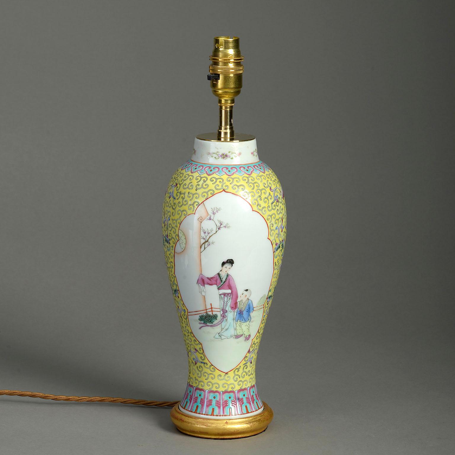 A late 19th century famille rose porcelain baluster vase, with figurative cartouches upon a yellow ground. Now mounted as a table lamp upon a hand-turned giltwood base.

Dimensions refer to vase and gilded base only.

Shade for display purposes