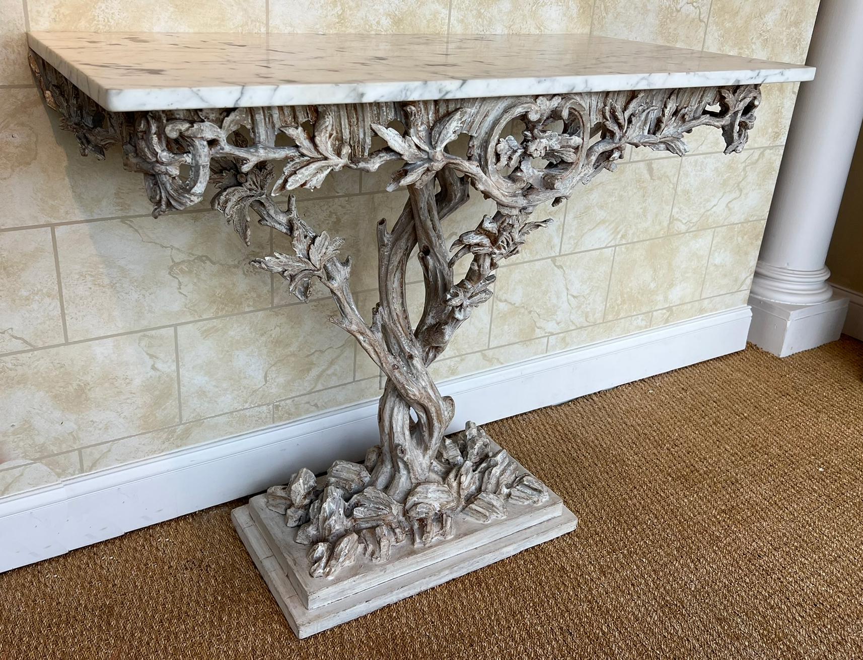 Console arboricole de style Fantasy Furniture, avec un plateau rectangulaire en marbre de Carrare, sur une base en bois sculpté à la main, avec une finition peinte, montrant une usure naturelle ; la base de la table est façonnée comme des branches
