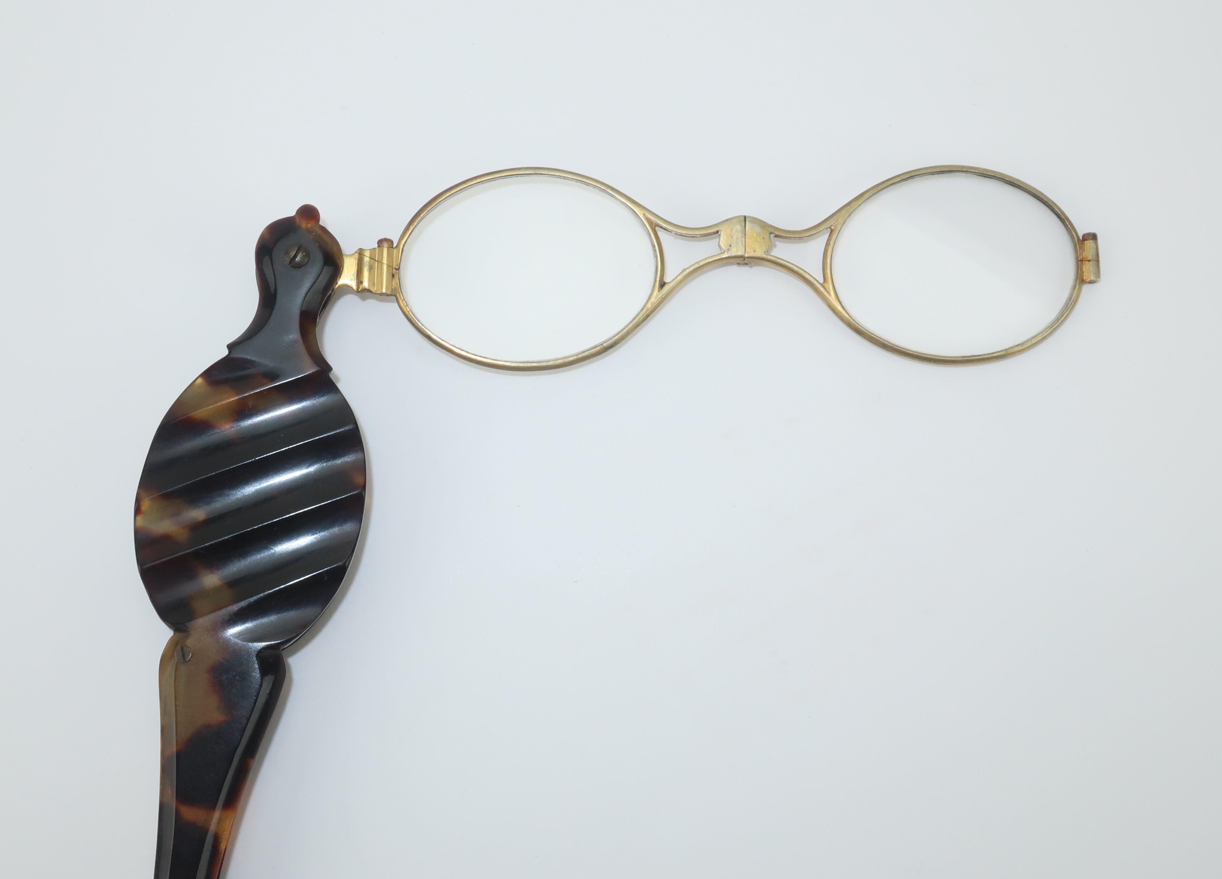 Late 19th Century imitation tortoise lorgnette magnifier glasses with a spring loaded mechanism for easy folding and storage.  The gold tone metal frames fold open by depressing a button on the handle shaft, shown in photograph 6.  A ring at the end