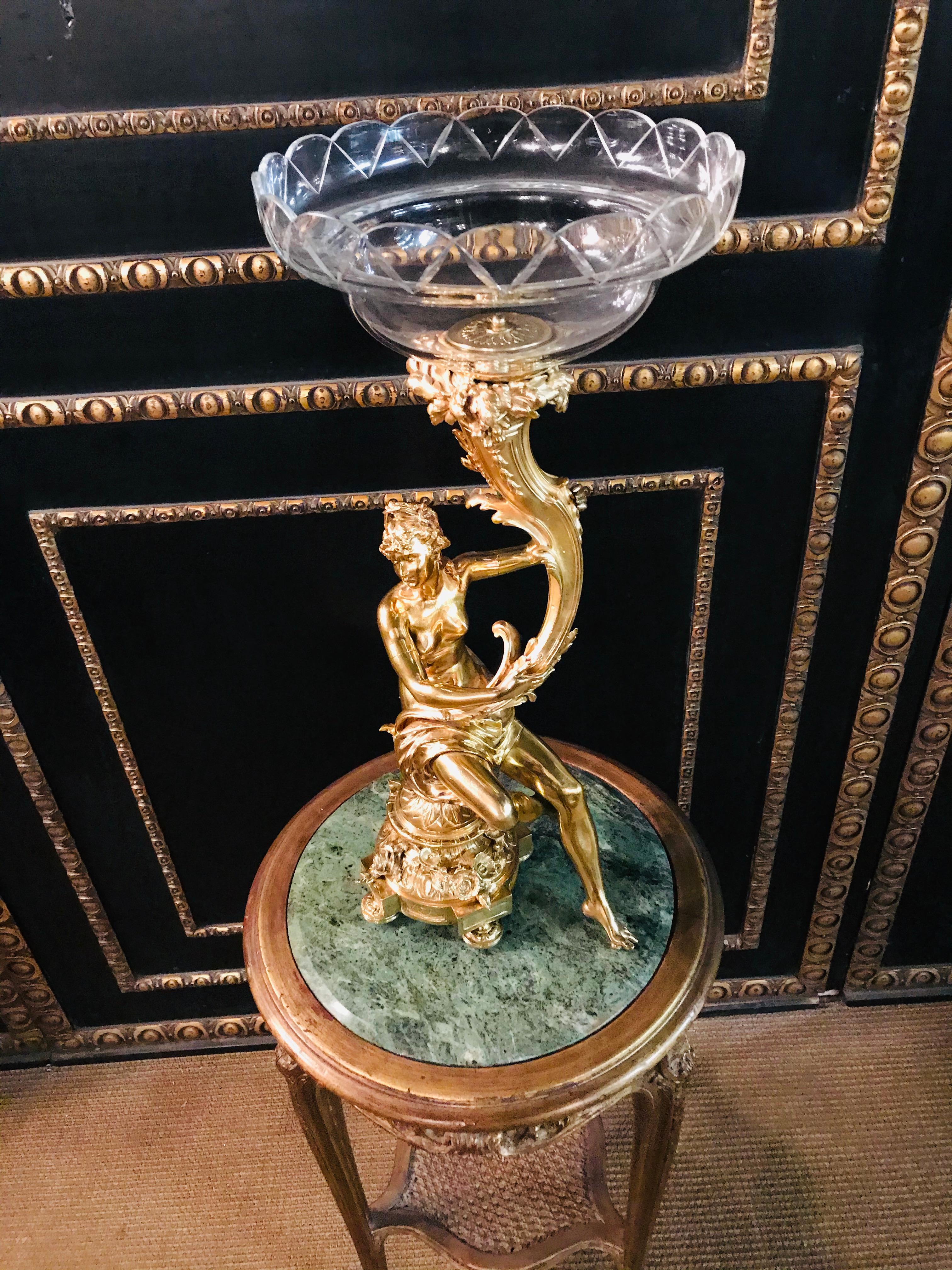 Very large figural centerpiece, 19th century polished brass. Profiled and ornamented pedestal with garlands. Sitting on it a naked beautiful woman, one foot on a small ball. Holding a cornucopia covered in foliage in his hands. Glass bowl attachment