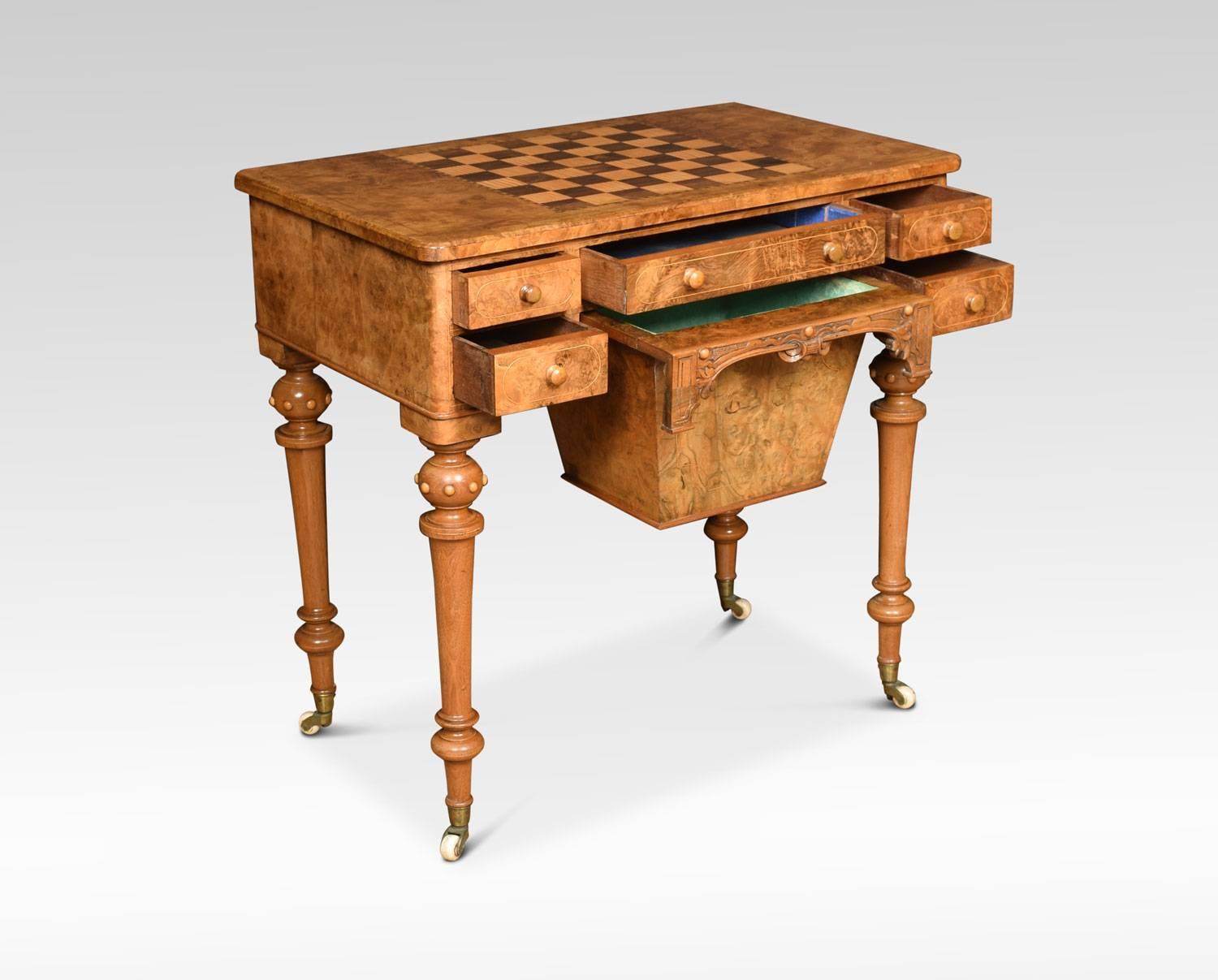 Victorian figured walnut inlaid games table, the chessboard top above an arrangement of five drawers surrounding a large central pull out basket. The games table raised on ring turned and tapering fluted supports with brass caps and ceramic