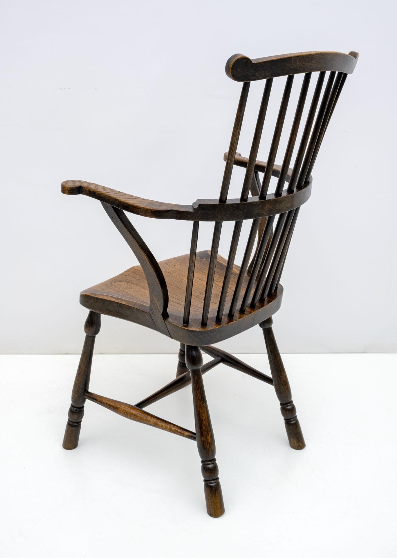 A beautiful 19th century English ash and oak scallop-back Windsor chair with outward facing arms supported by inverted stretchers, turned legs connected by a bentwood stretcher and a solid oak seat. The seat is a piece of wood with a nice patina and